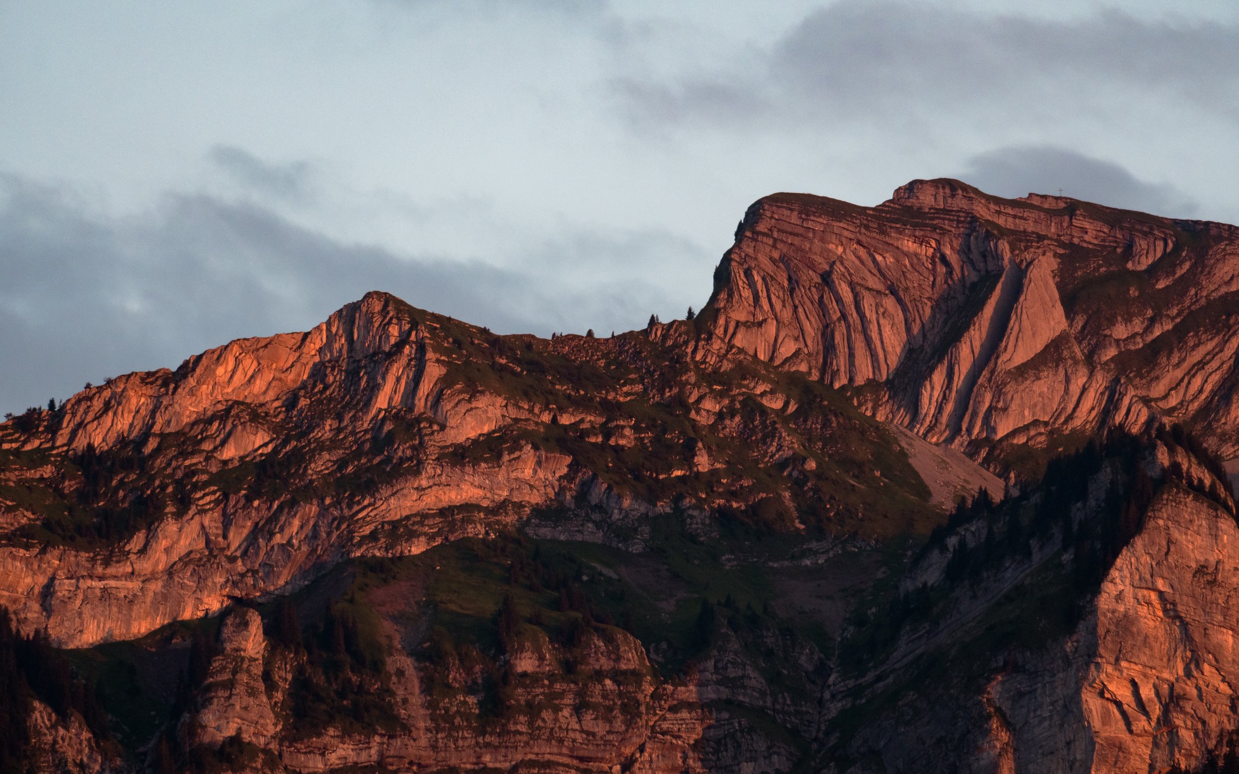 Sunset illuminating rugged mountain peaks and cliffs with a cloudy sky in the background.