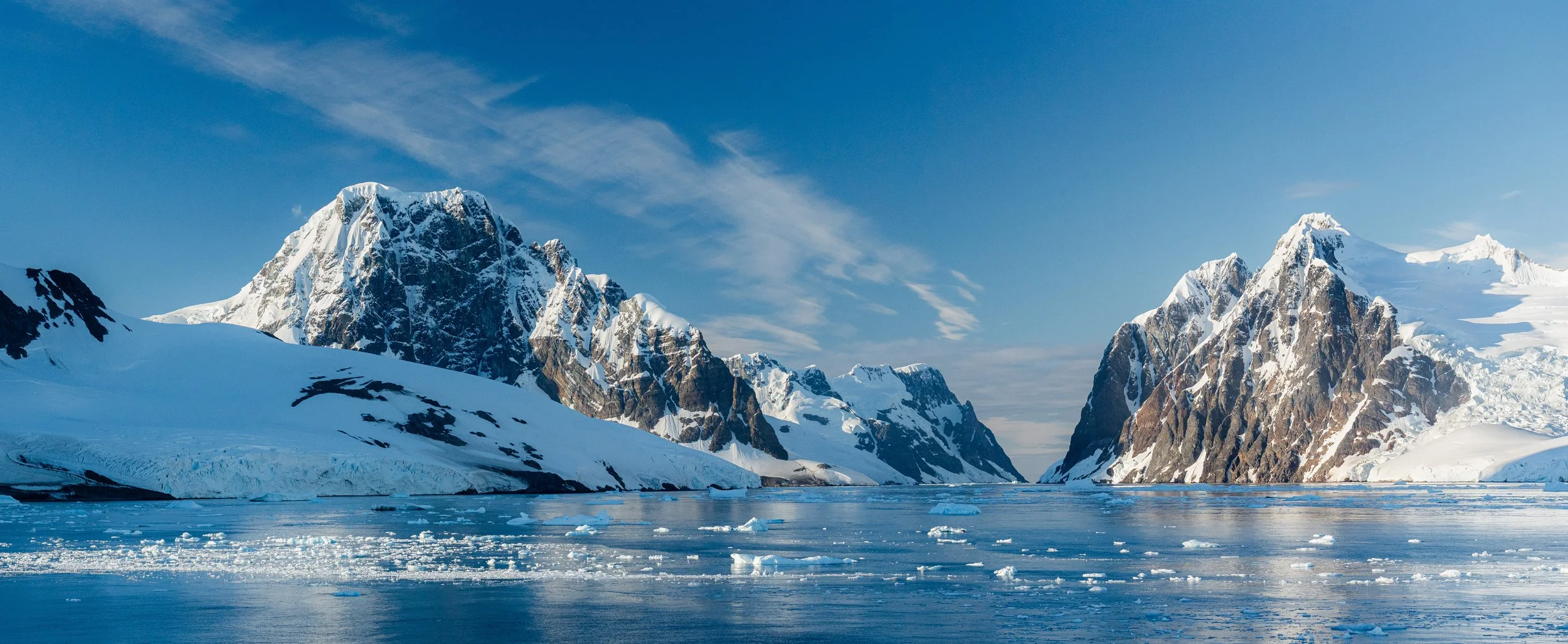 Snow-covered mountains and icy water under a partly cloudy sky during daytime.