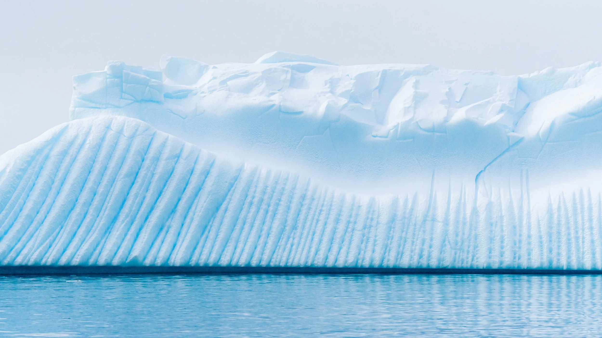 Close-up of a large iceberg with textured ice formations, floating in calm icy water.