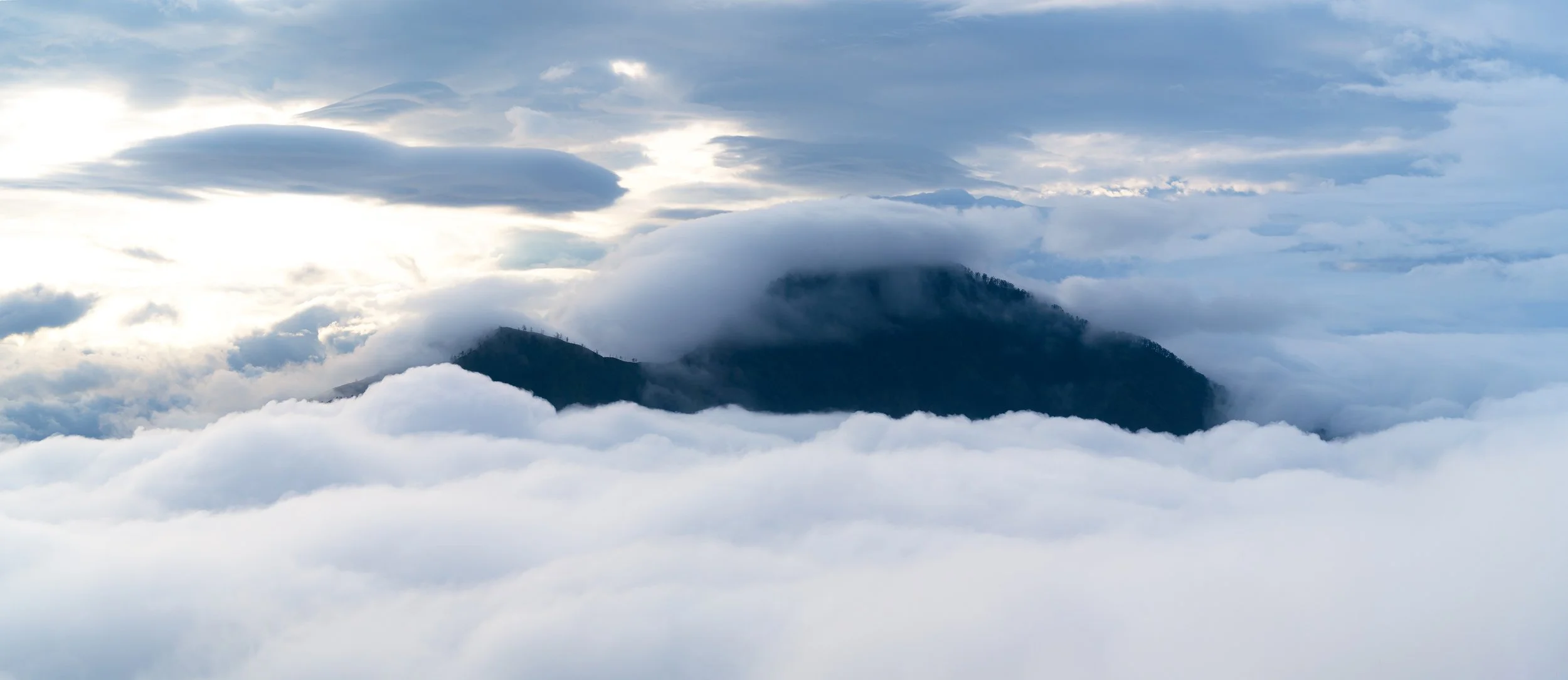 Mountains surrounded by dense clouds and mist, with a partly cloudy sky.