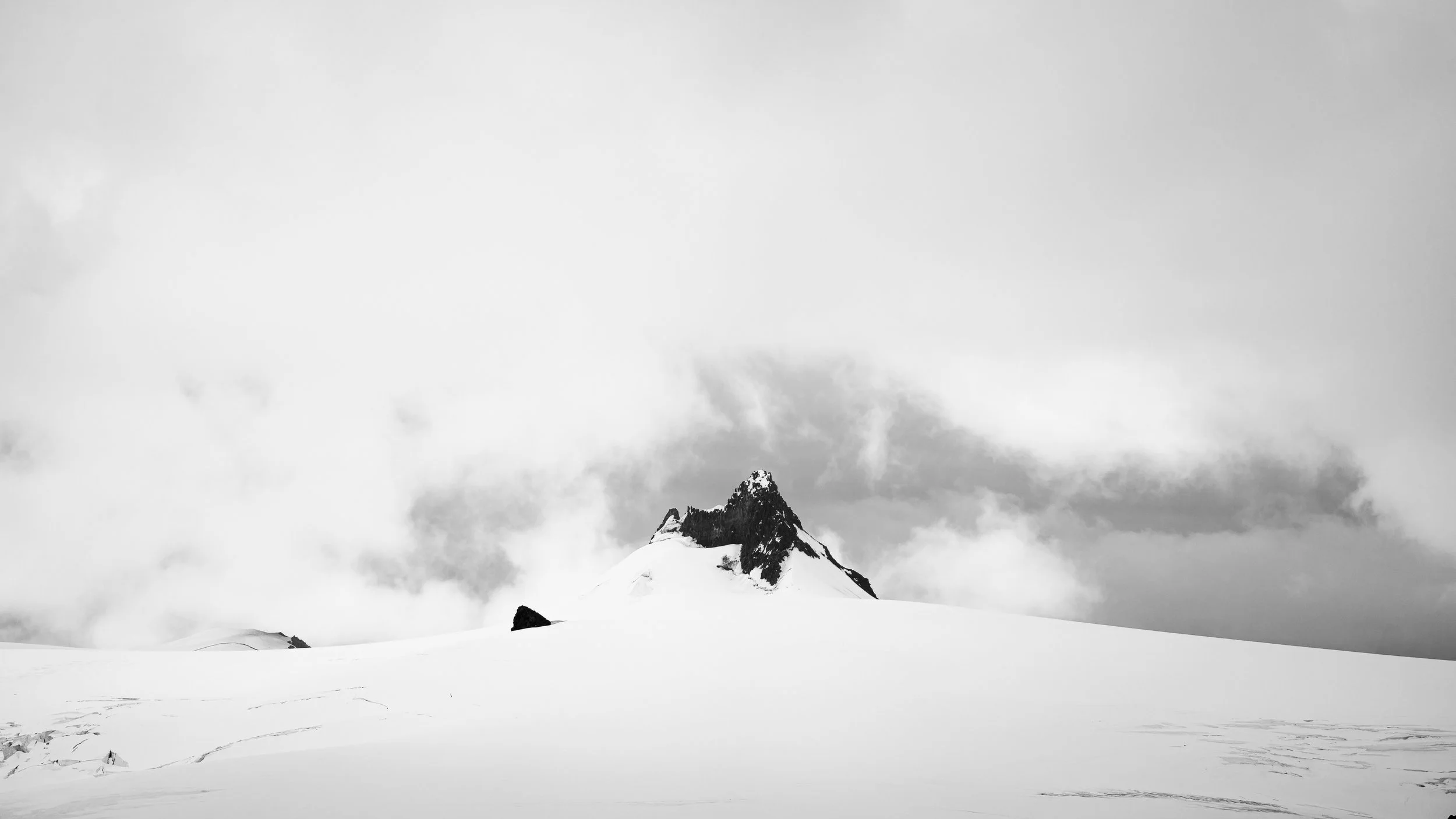 Snow-covered mountain peak rising above a cloudy sky in black and white