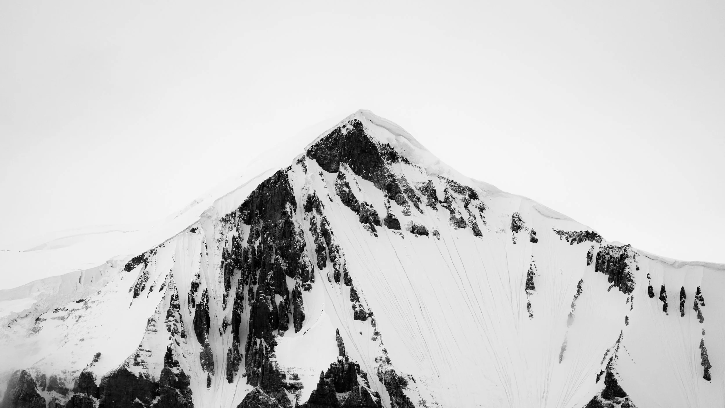 Black and white photo of a snow-covered mountain peak with steep rocky slopes.