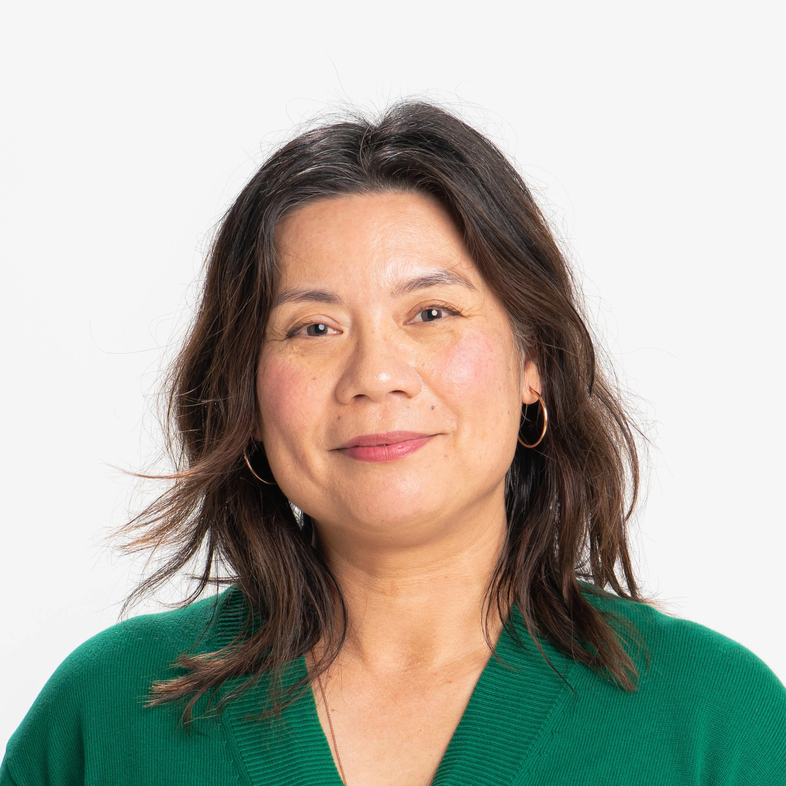 Close-up of a woman with shoulder-length dark brown hair wearing a green sweater, smiling softly, against a plain white background.