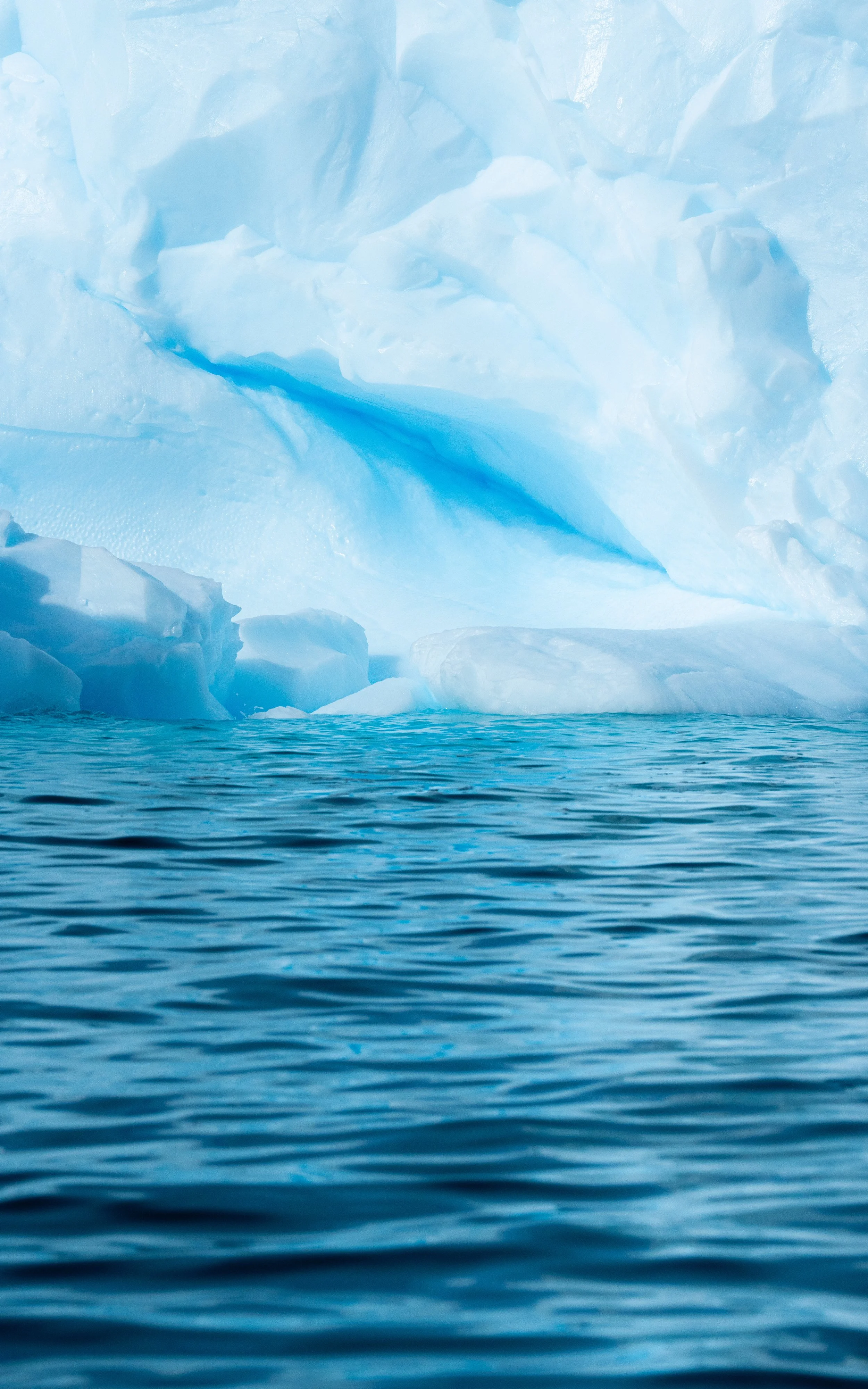 A large iceberg floating in cold ocean water with blue ice formations above and below the water line.