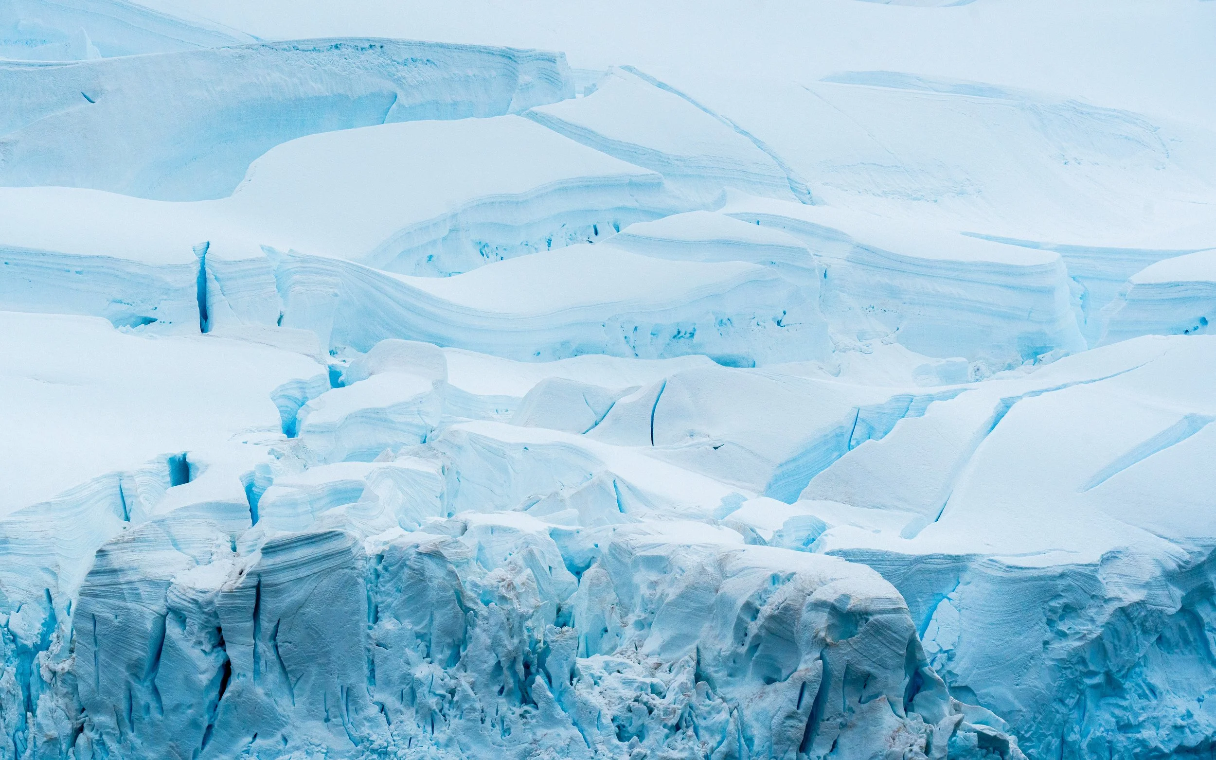 A large glacier with jagged ice formations and visible cracks, surrounded by snow and ice.