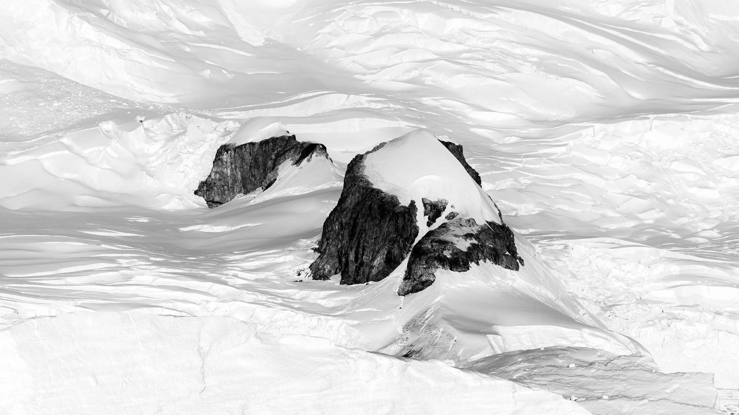 Snow-covered mountainous landscape with large rocks protruding from the snow, black and white photograph.