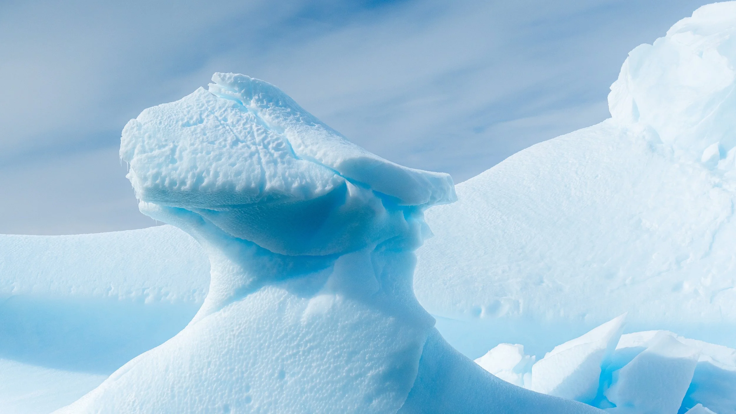 Large blue ice formation in a snowy landscape under a partly cloudy sky.