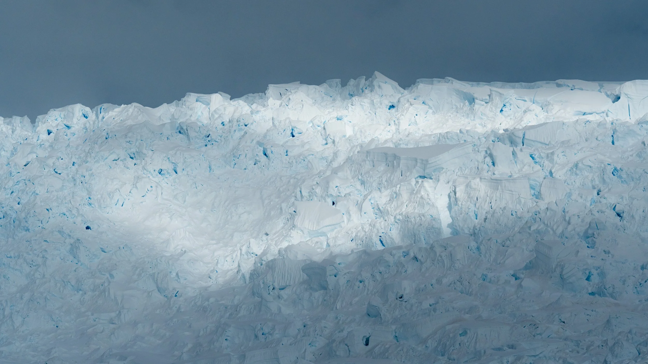 A large glacier with jagged ice formations and a dark, cloudy sky above.