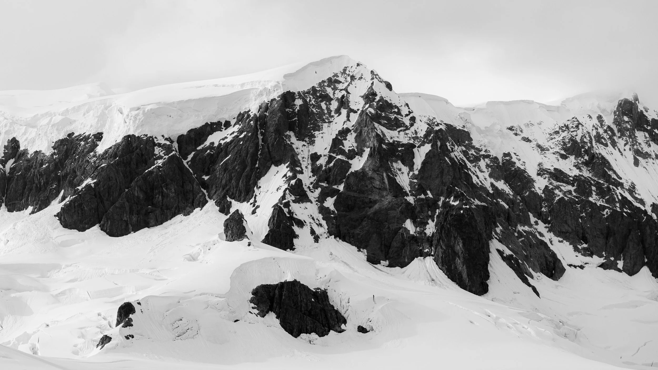 Snow-covered mountain range with rugged dark rock formations and glaciers.
