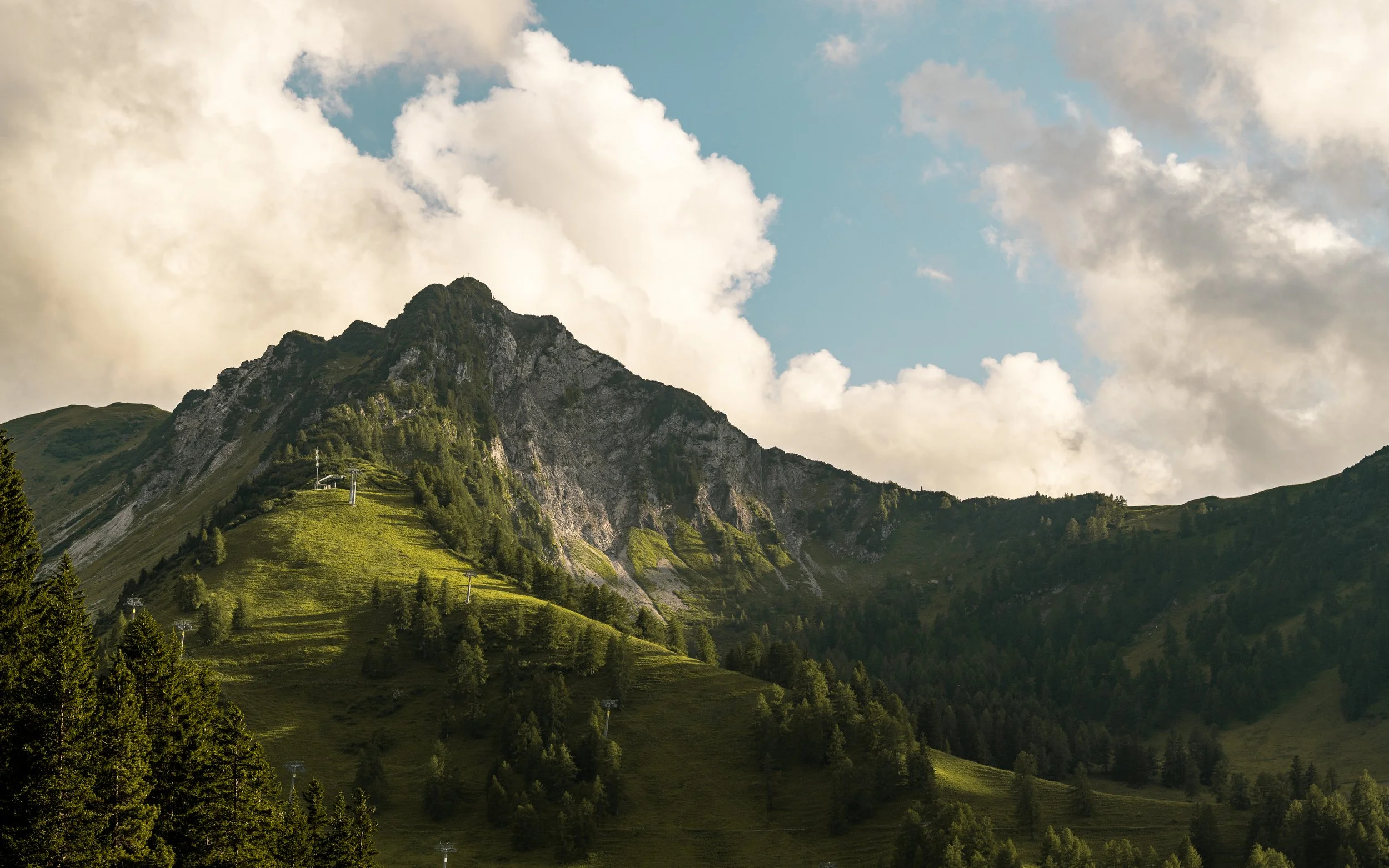 Mountain with lush green slopes and trees, under a partly cloudy sky.