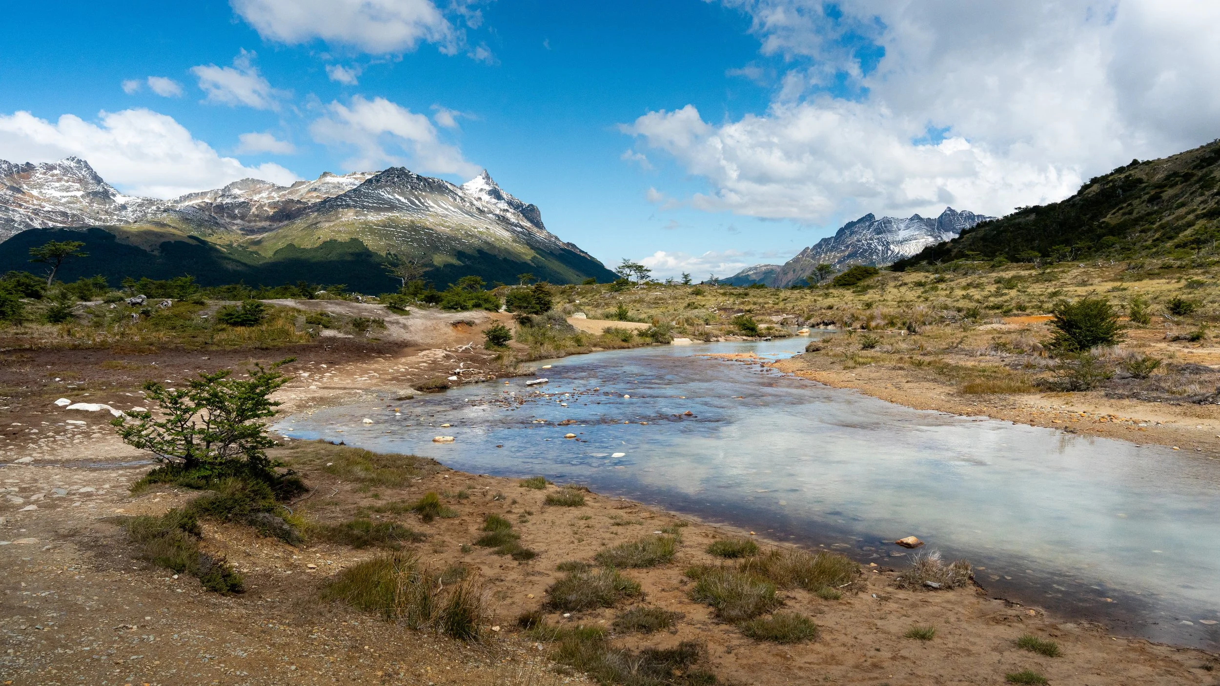 Mountains with some snow, trees, a body of water, and partly cloudy sky.