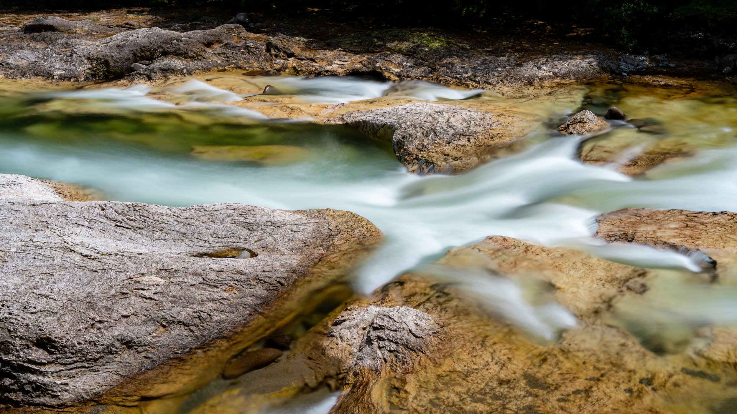 Flowing stream over rocks in a forested area, long exposure shot creating a smooth water effect.