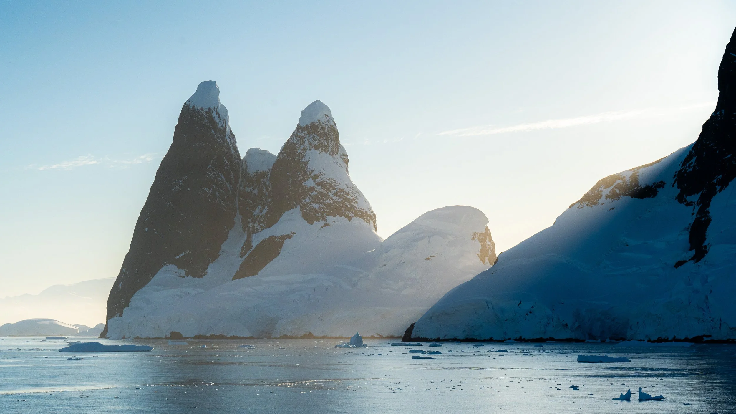 Snow-covered mountains and icebergs in a frozen body of water under a clear sky.