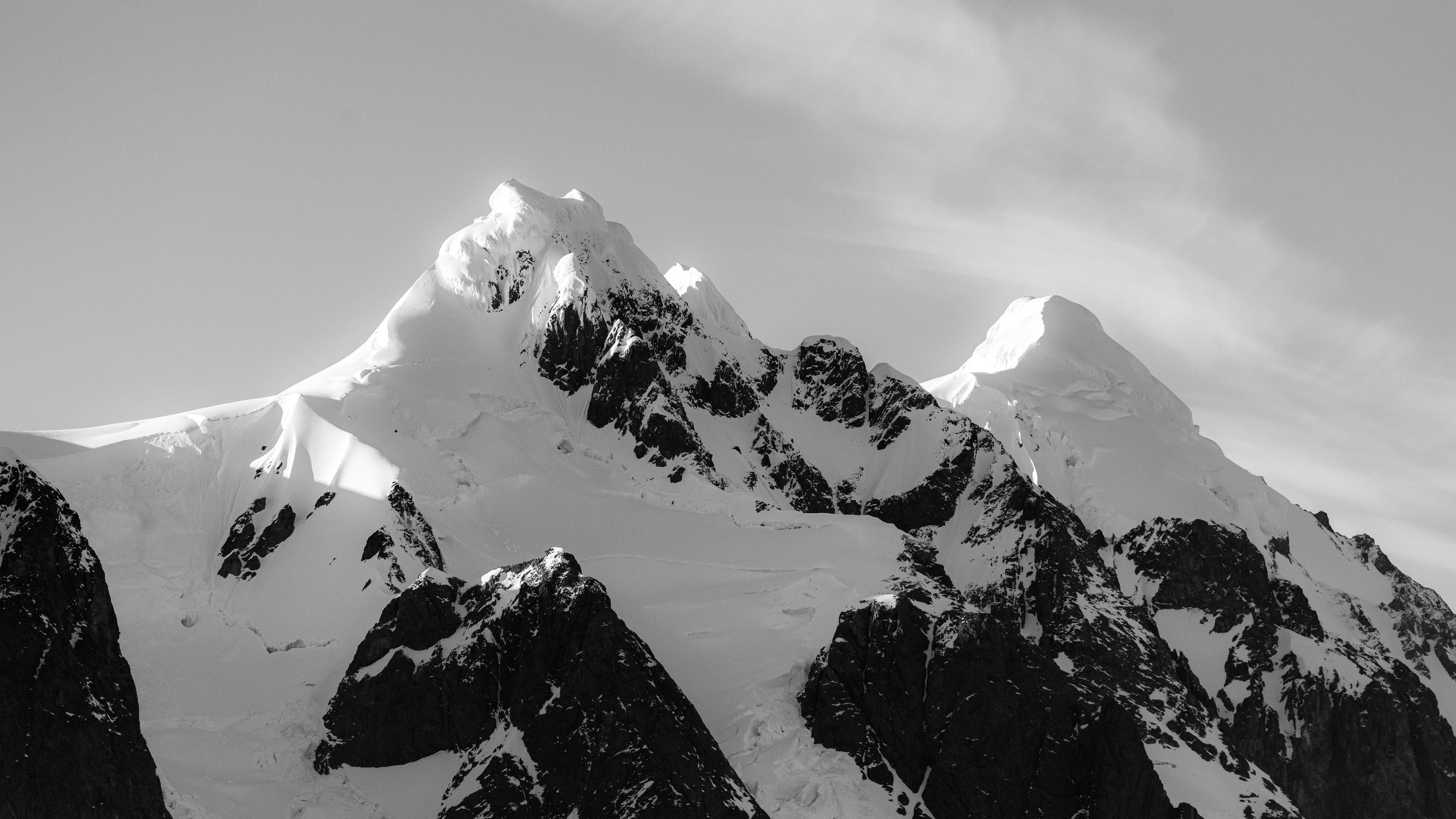 Snow-covered mountain peaks in a grayscale image with clouds in the sky