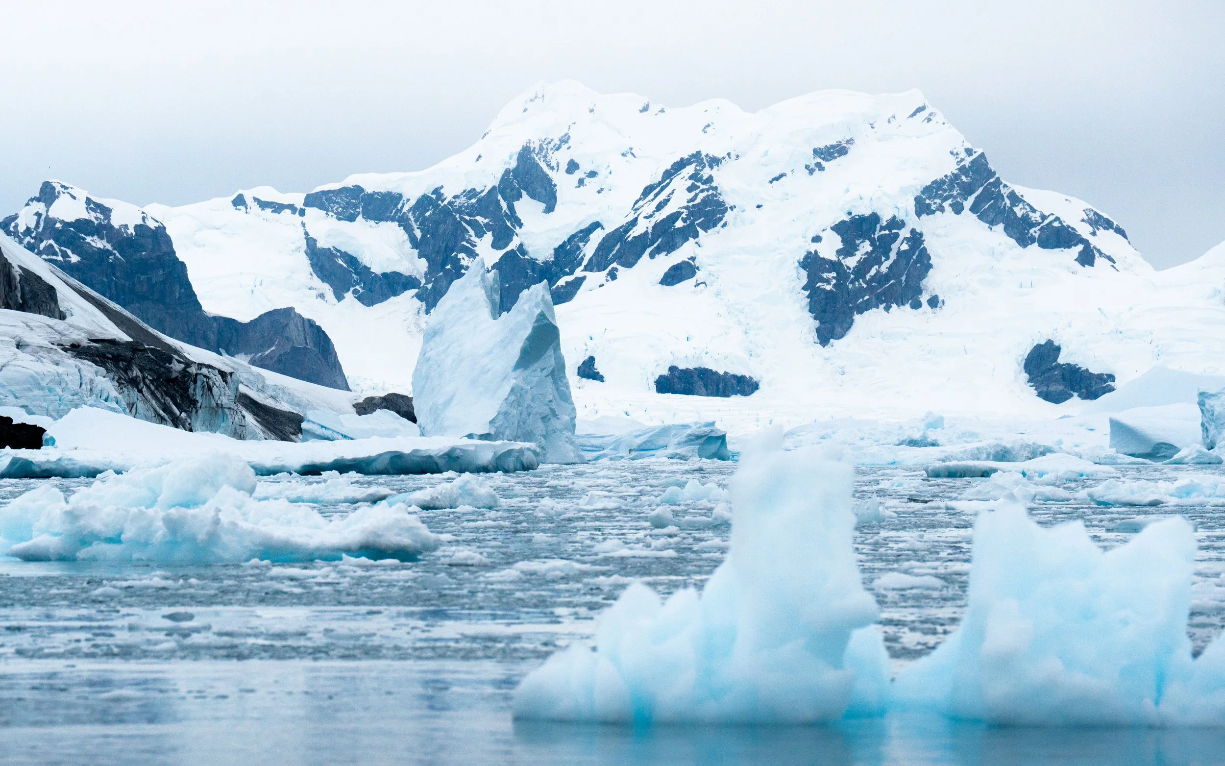 A snowy mountain landscape with icebergs floating in cold water.