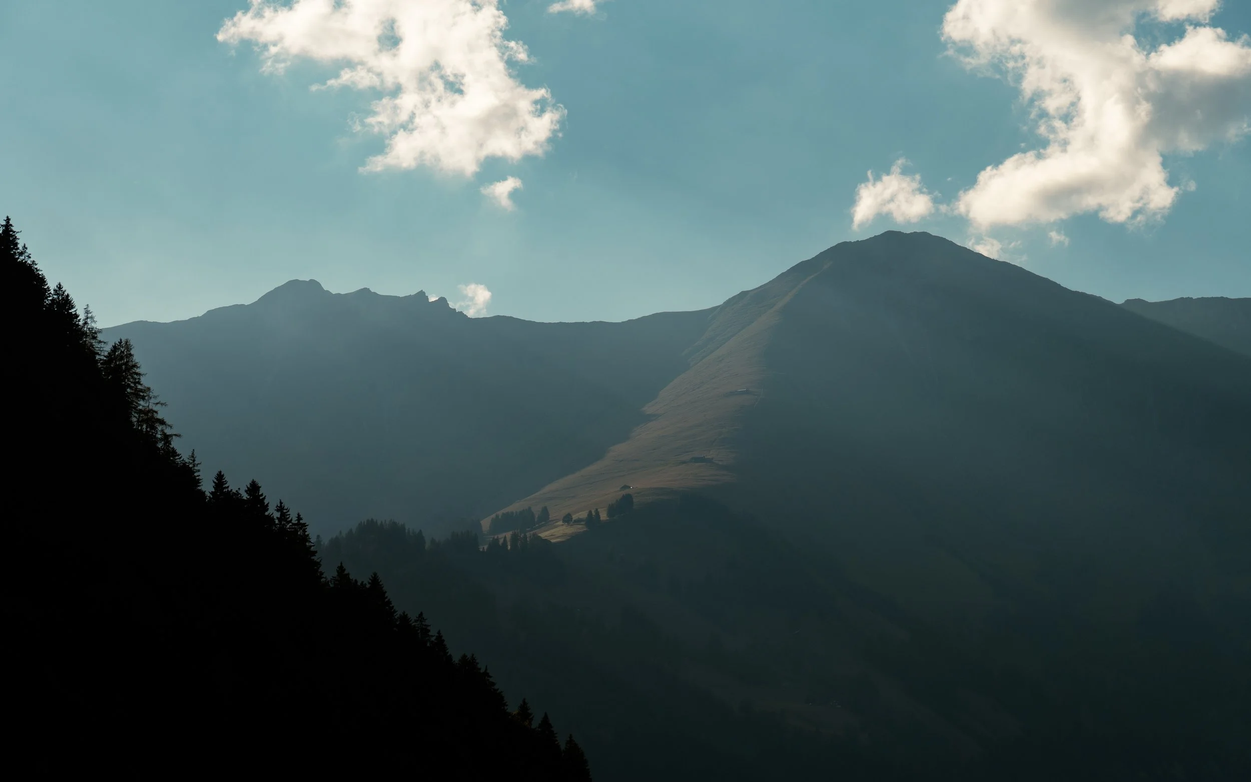 Scenic view of mountain range with partly cloudy sky, dark silhouette of trees in foreground.