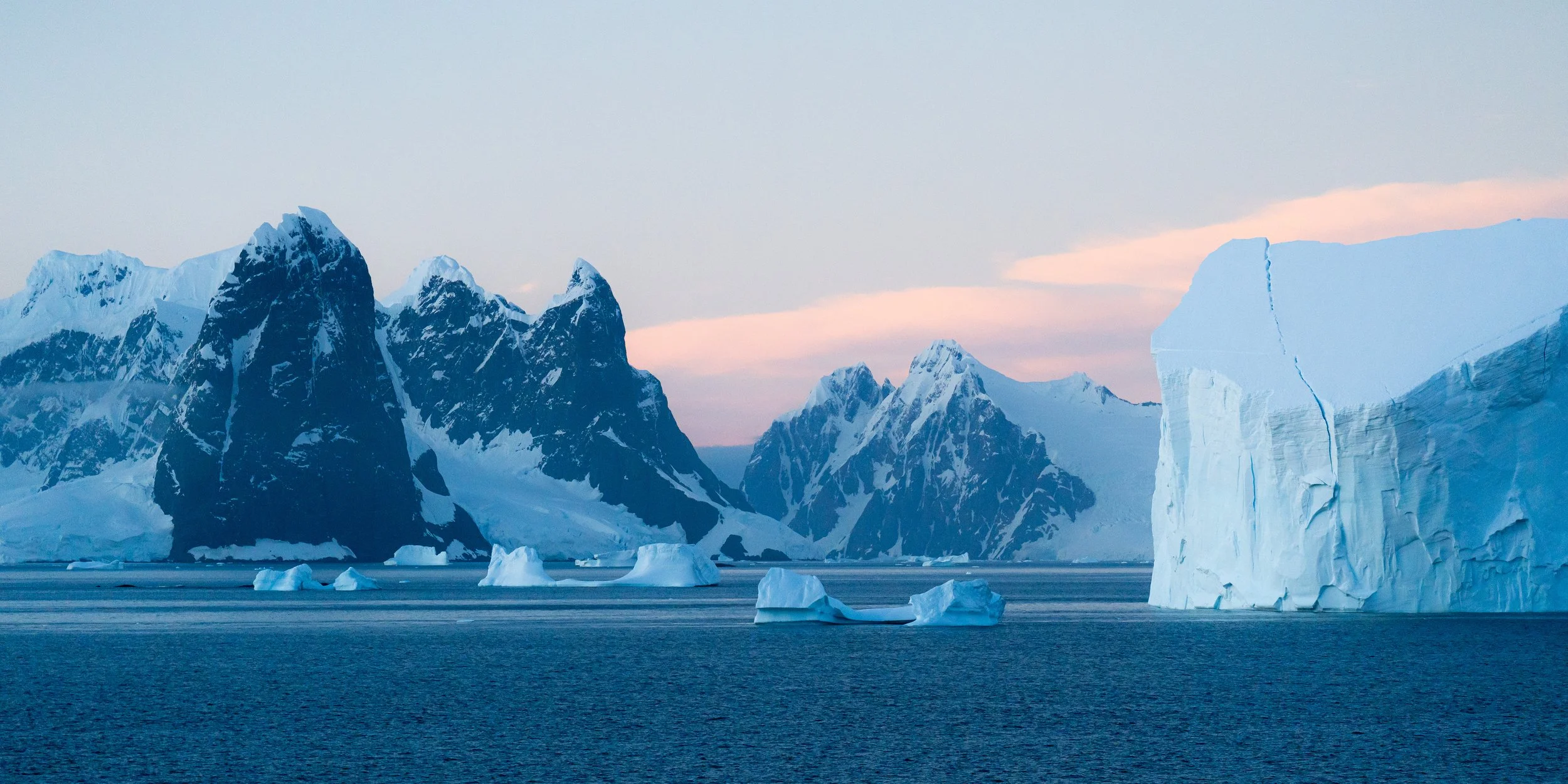 Icebergs floating in the water with snow-covered mountains in the background