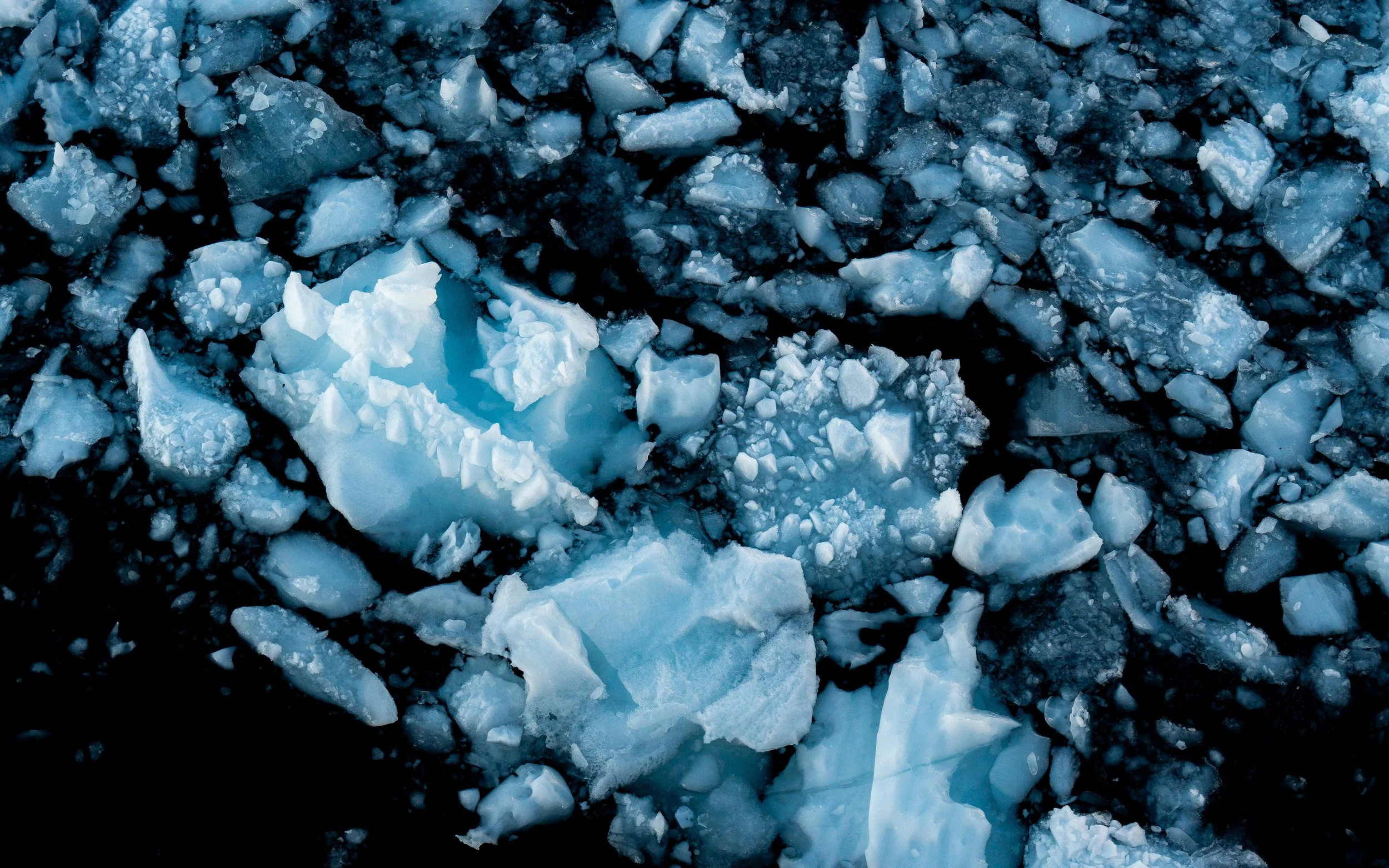 A close-up view of broken ice chunks on a dark surface, with some ice appearing blue.