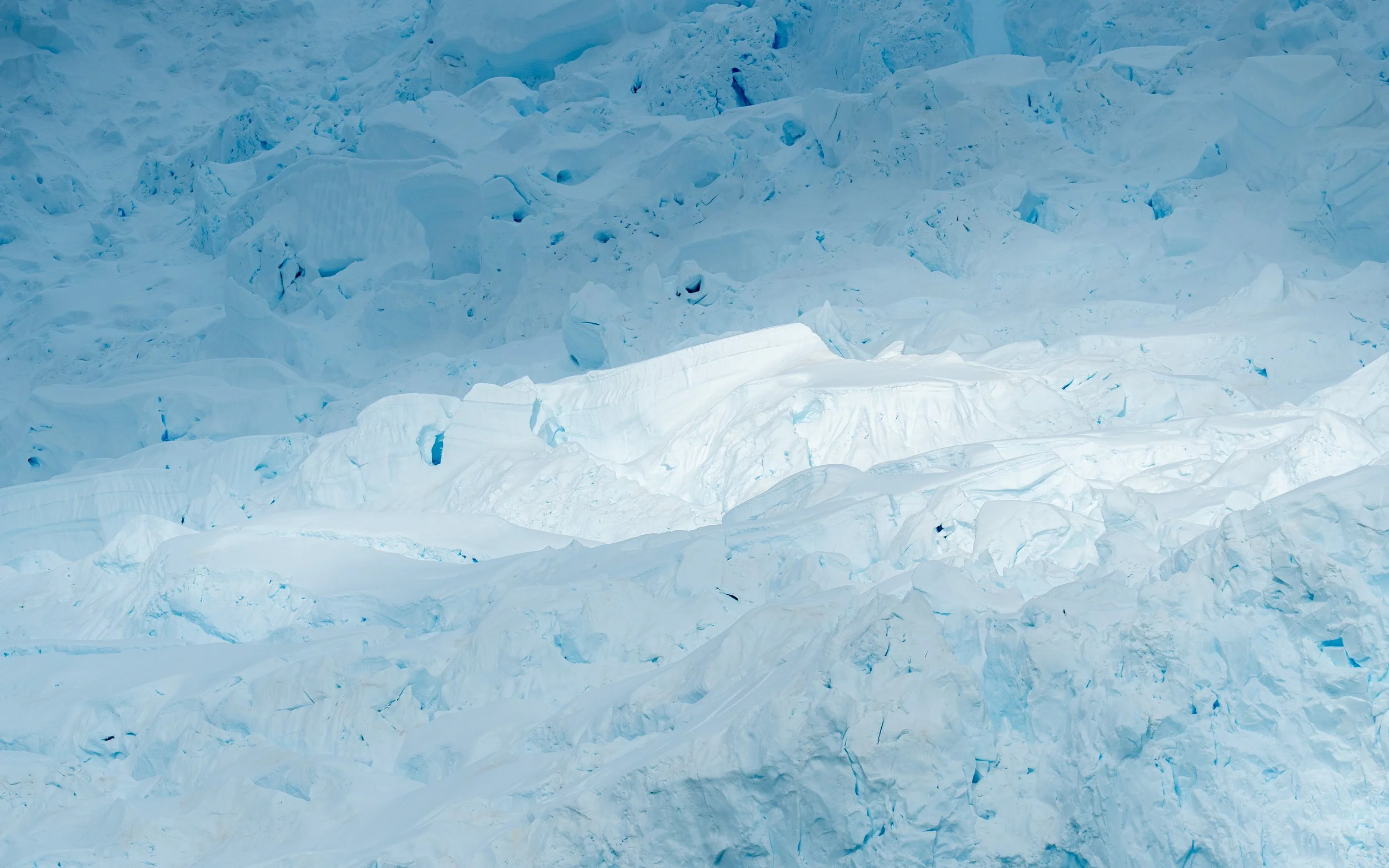 A vast expanse of snow and ice, with jagged ice formations and deep crevasses.