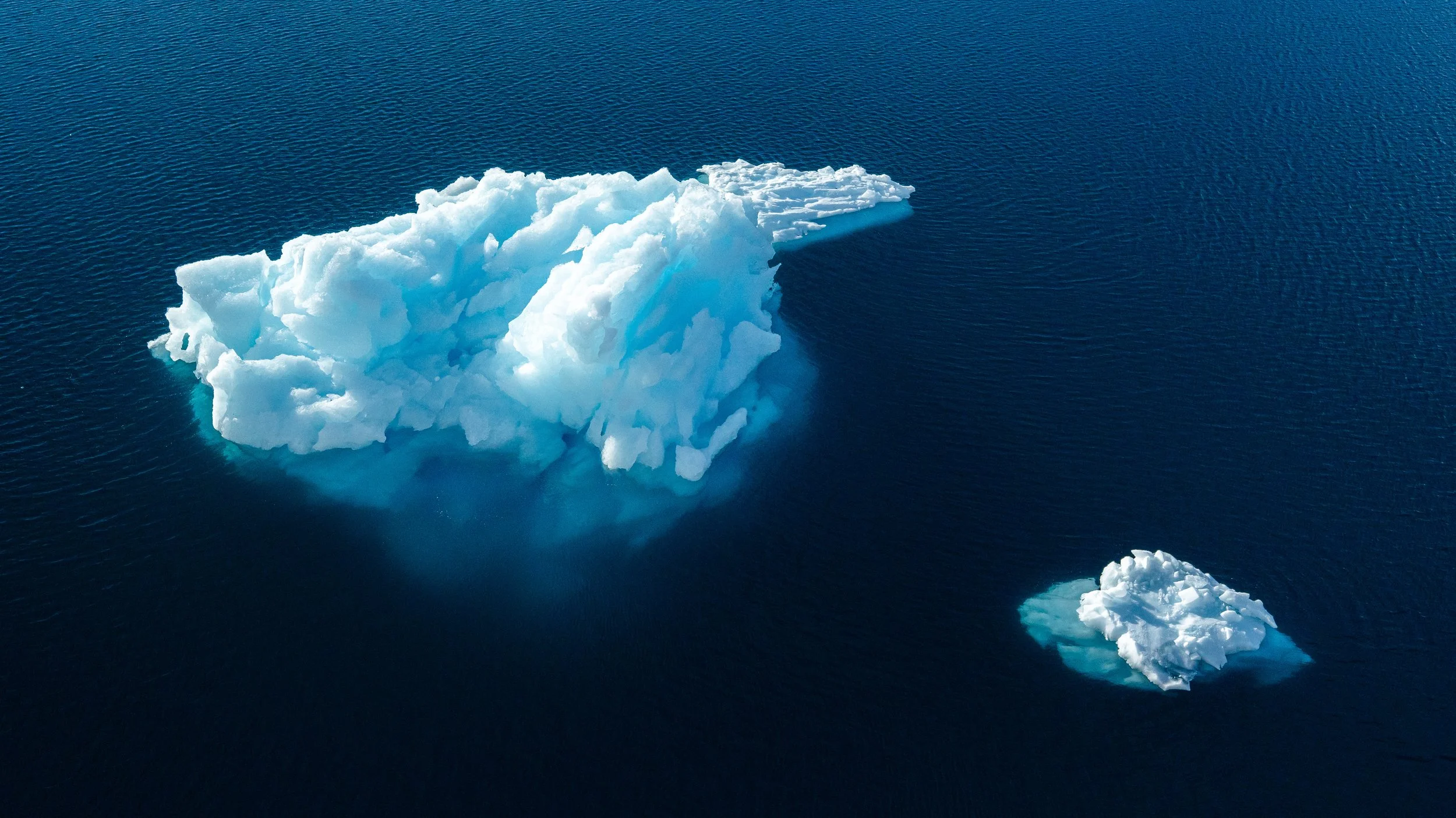 A large iceberg floating in the ocean with a smaller piece nearby.