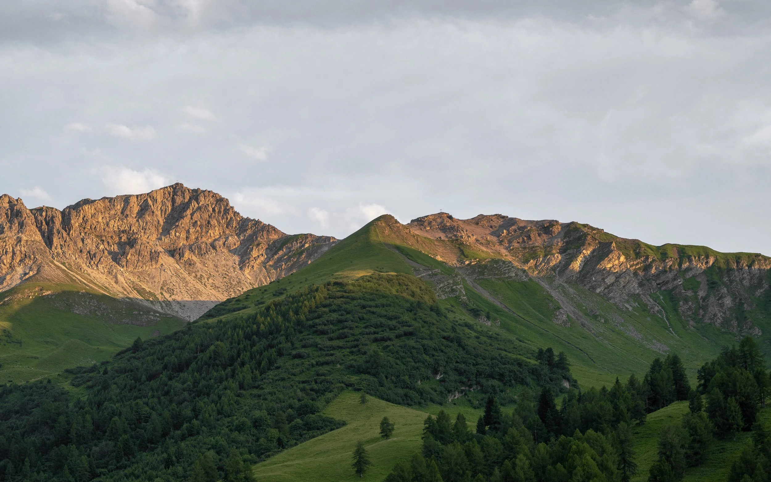 Scenic view of a mountain range with rocky peaks and green slopes under a partly cloudy sky.
