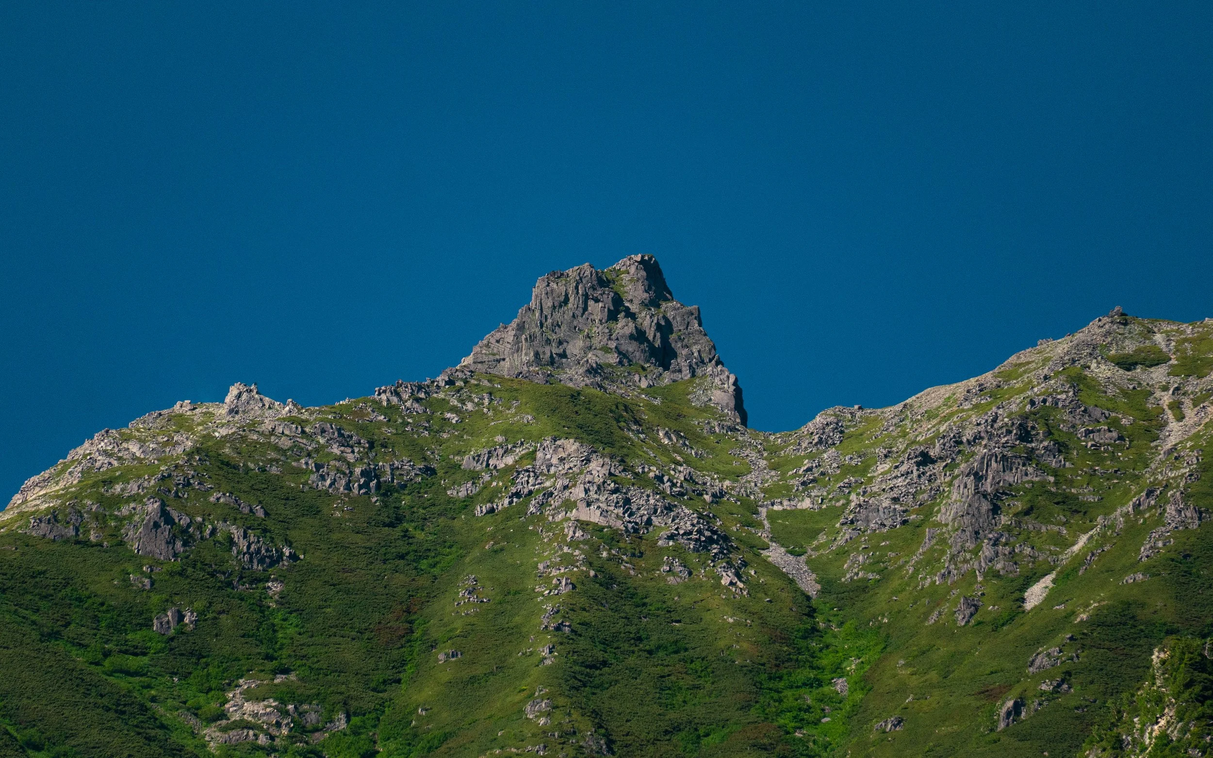 A mountain with rocky peaks and green slopes under a clear blue sky.