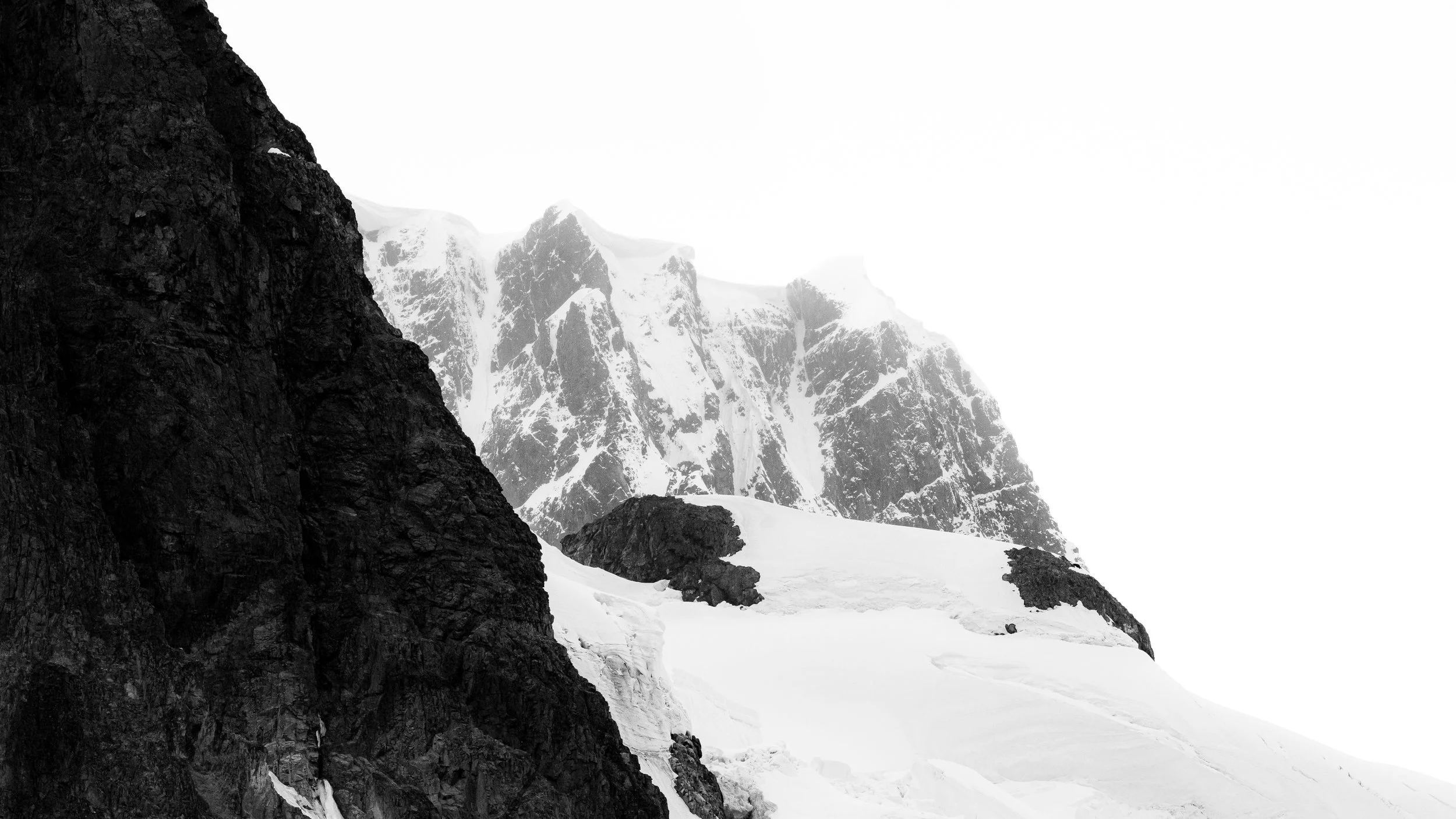 Snow-covered mountain peaks with a dark rocky cliff in the foreground.