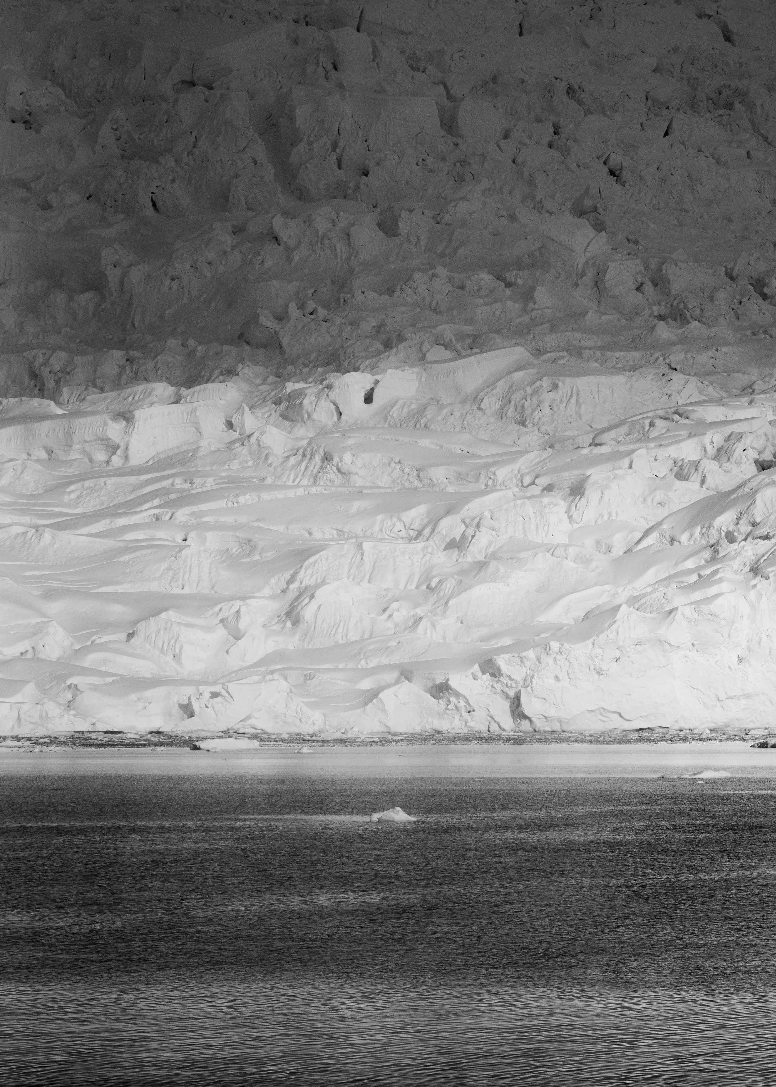 Black and white photograph of a snow-covered mountain with a frozen body of water in the foreground.