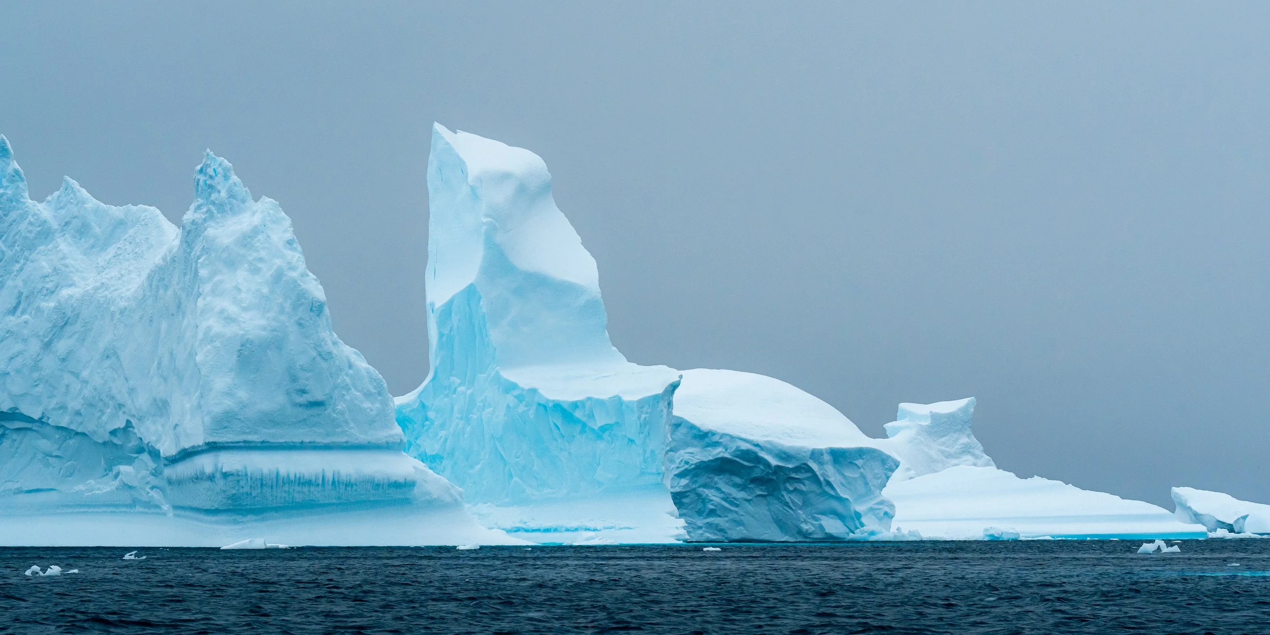 Large iceberg floating in icy ocean under cloudy sky.