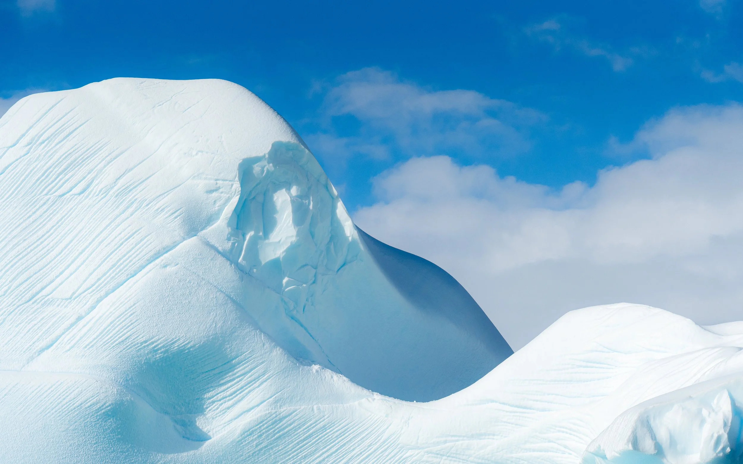 Snow-covered mountain peak against a partly cloudy blue sky.
