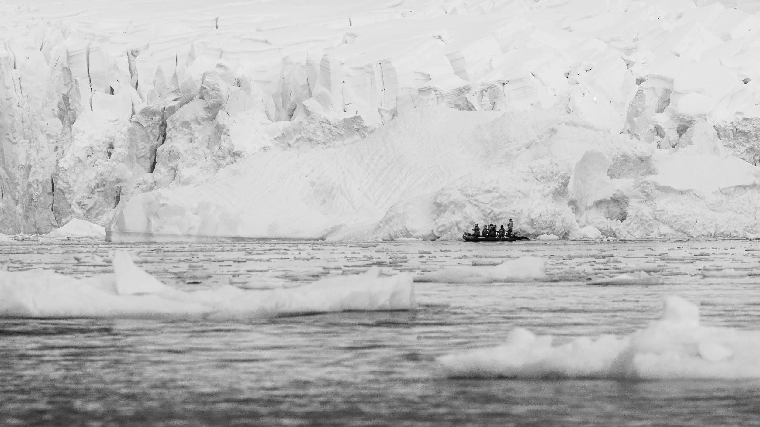 A small boat with multiple people in cold, icy waters near a large ice formation or glacier.