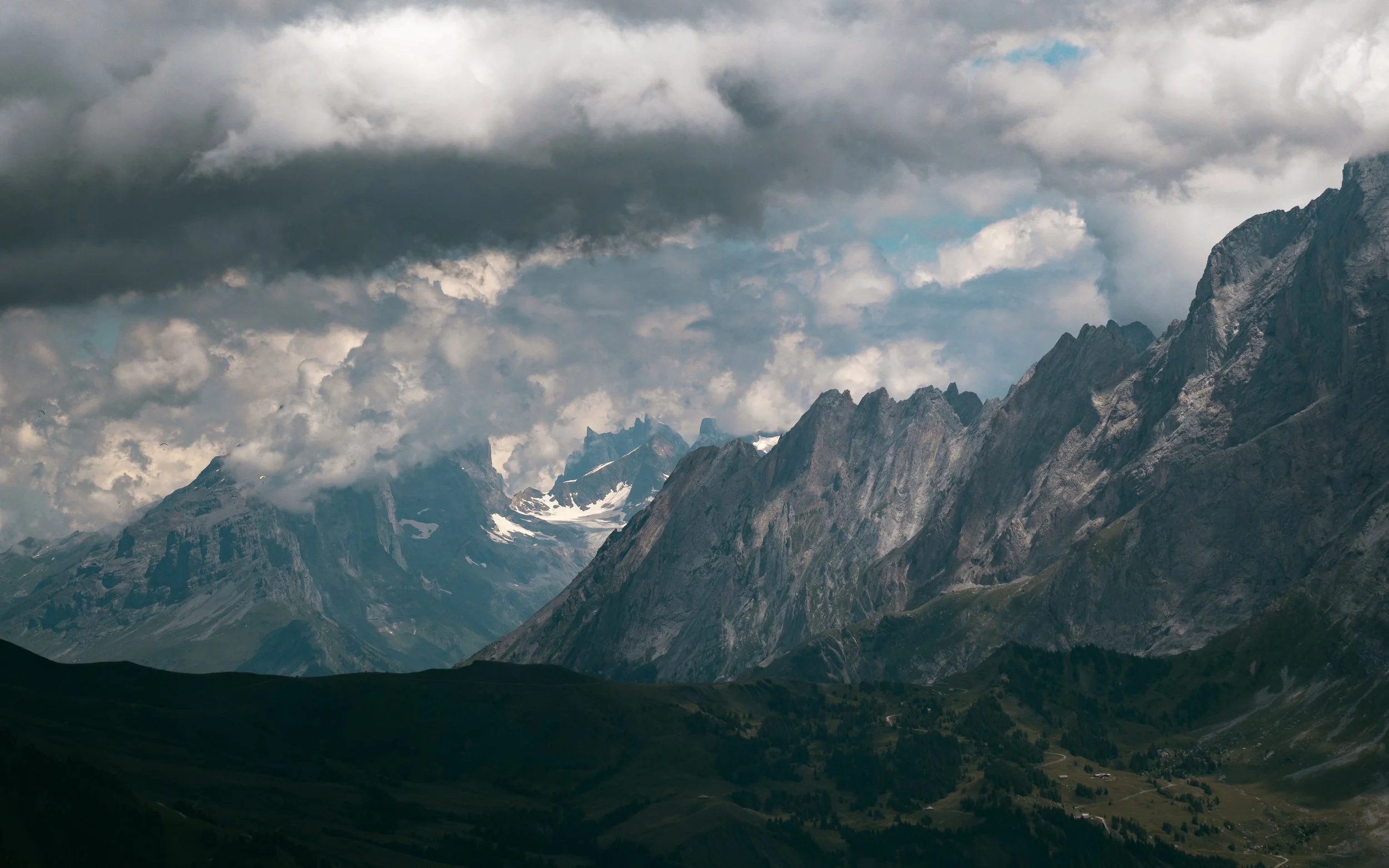 Mountain landscape with jagged peaks partially covered in snow, under a cloudy sky.