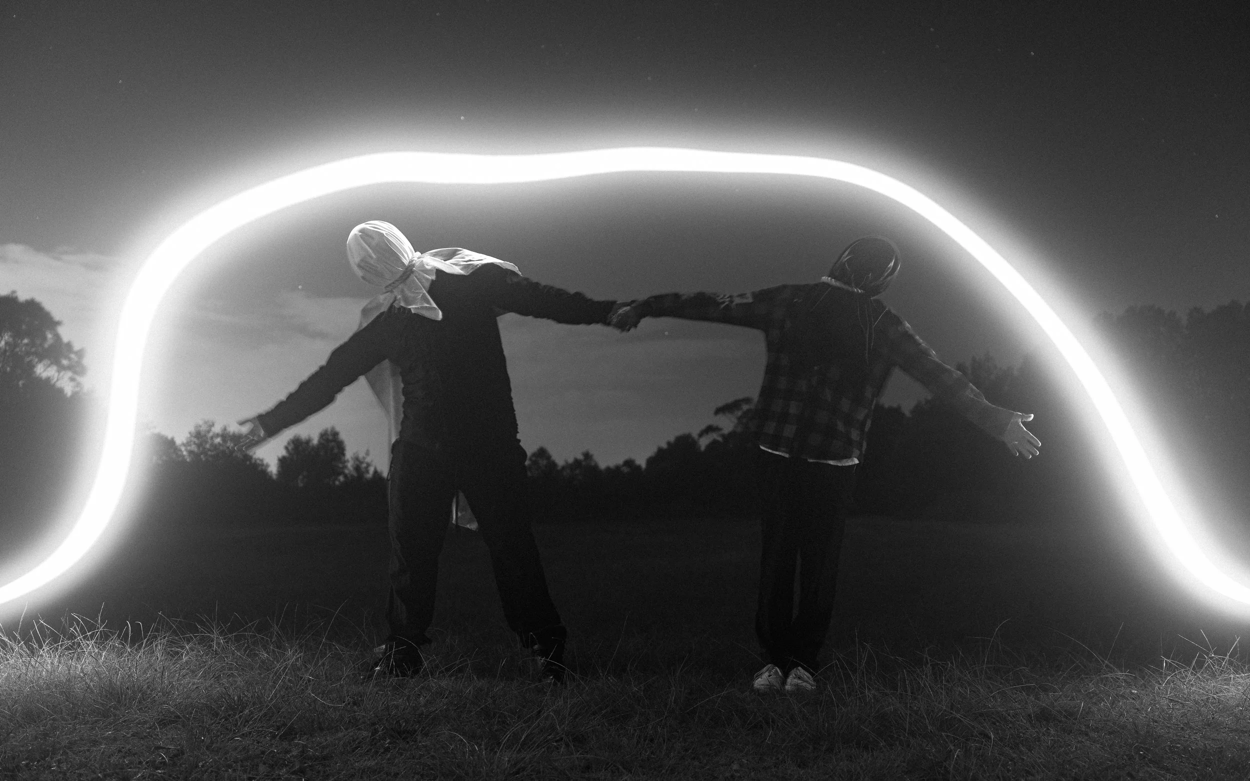 Two people standing outdoors at night holding hands, with a glowing circle of light behind them, creating a silhouette effect.