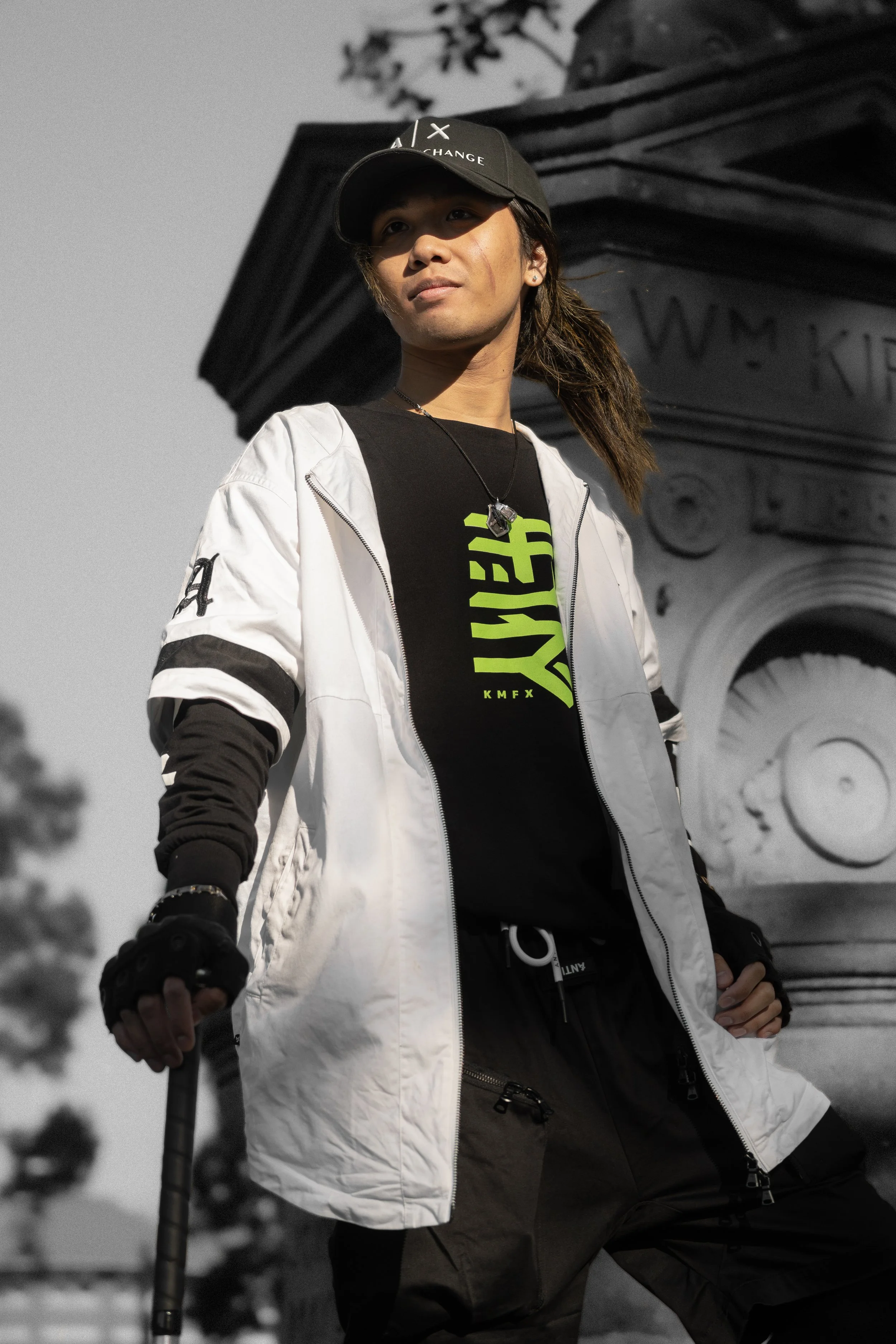 A woman standing outdoors near the Washington Monument, dressed in a white and black jacket, black gloves, and a black cap, with a cityscape background.