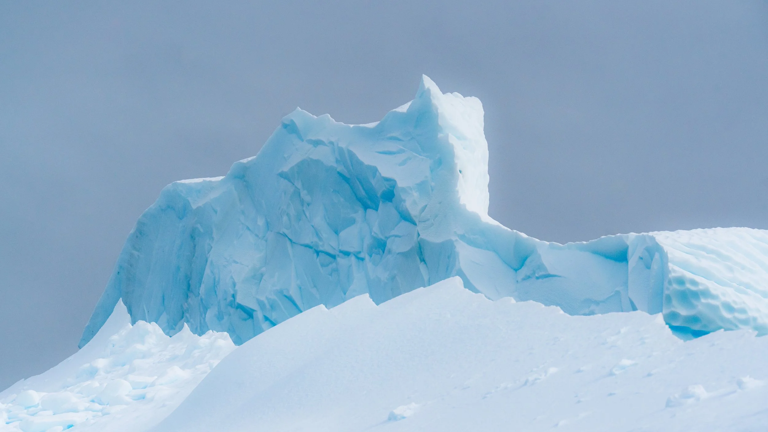 Large iceberg with jagged, sharp edges floating in the ocean on a cloudy day.