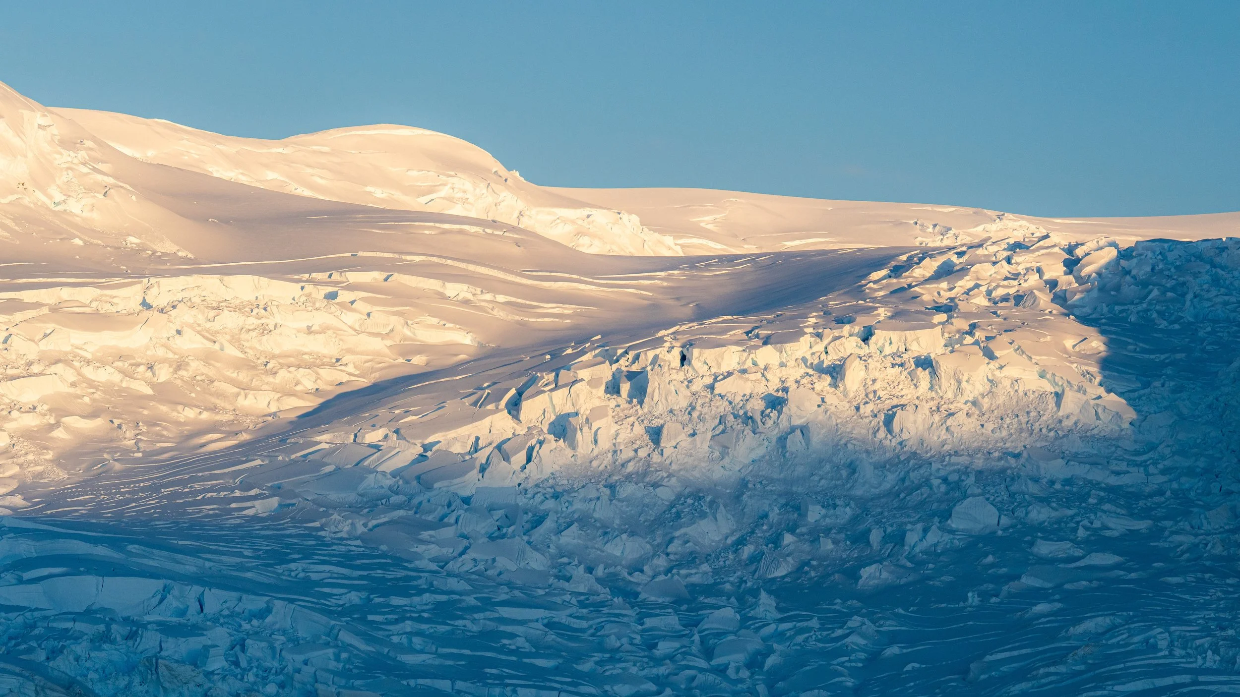 Snow-covered landscape with some ice formations and a clear blue sky.