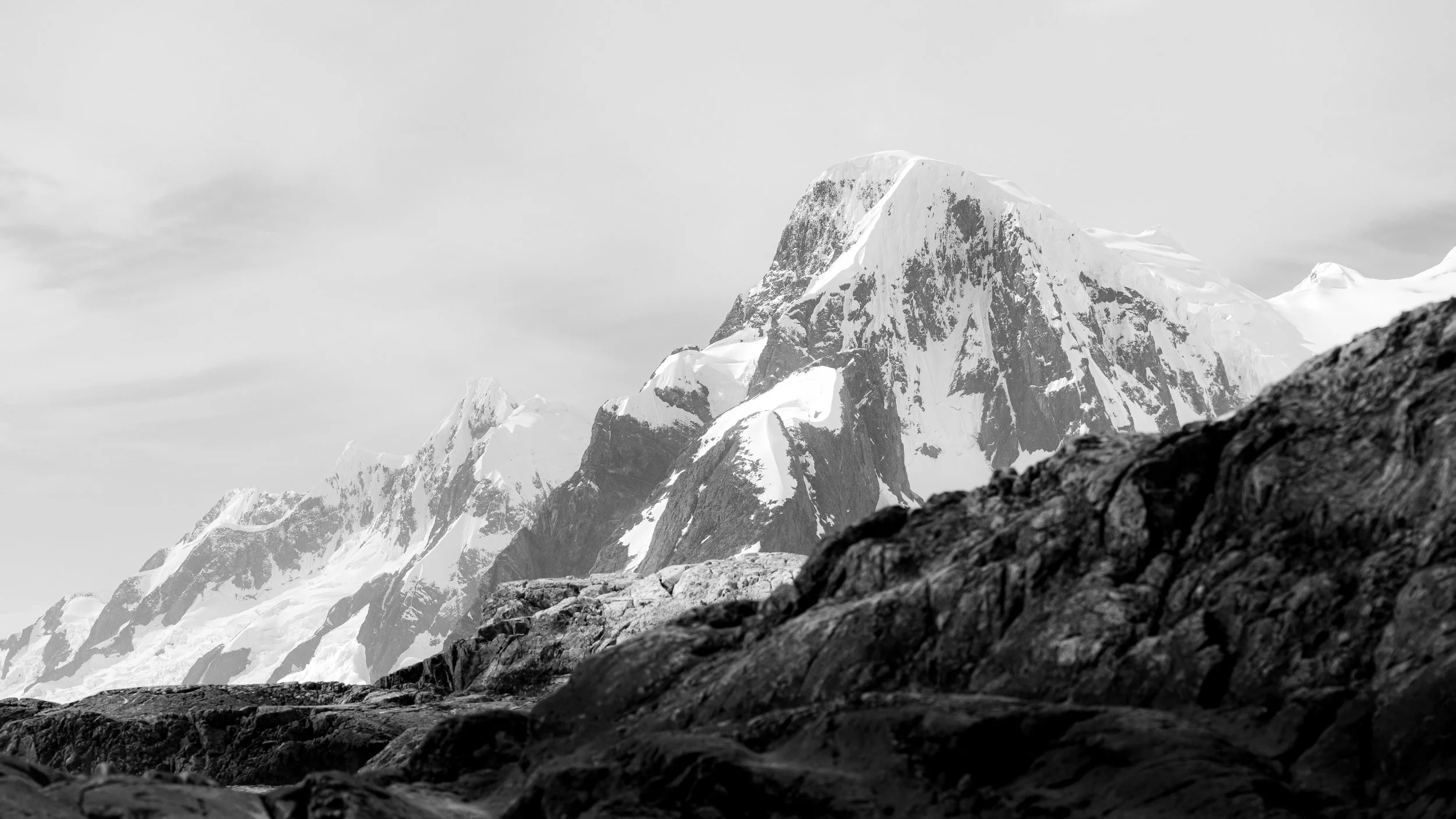 Snow-covered mountain peak with rugged rocks in the foreground, in black and white.