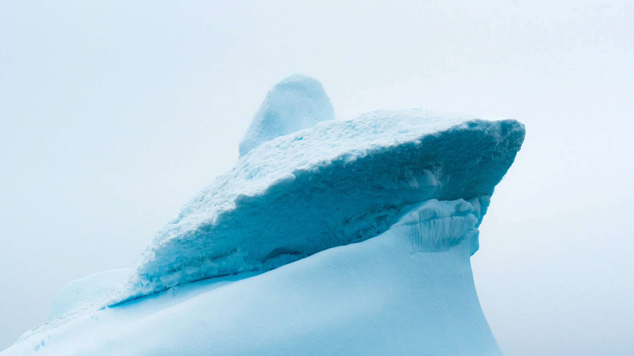 A large iceberg with a jagged surface floating in a cloudy, icy environment.