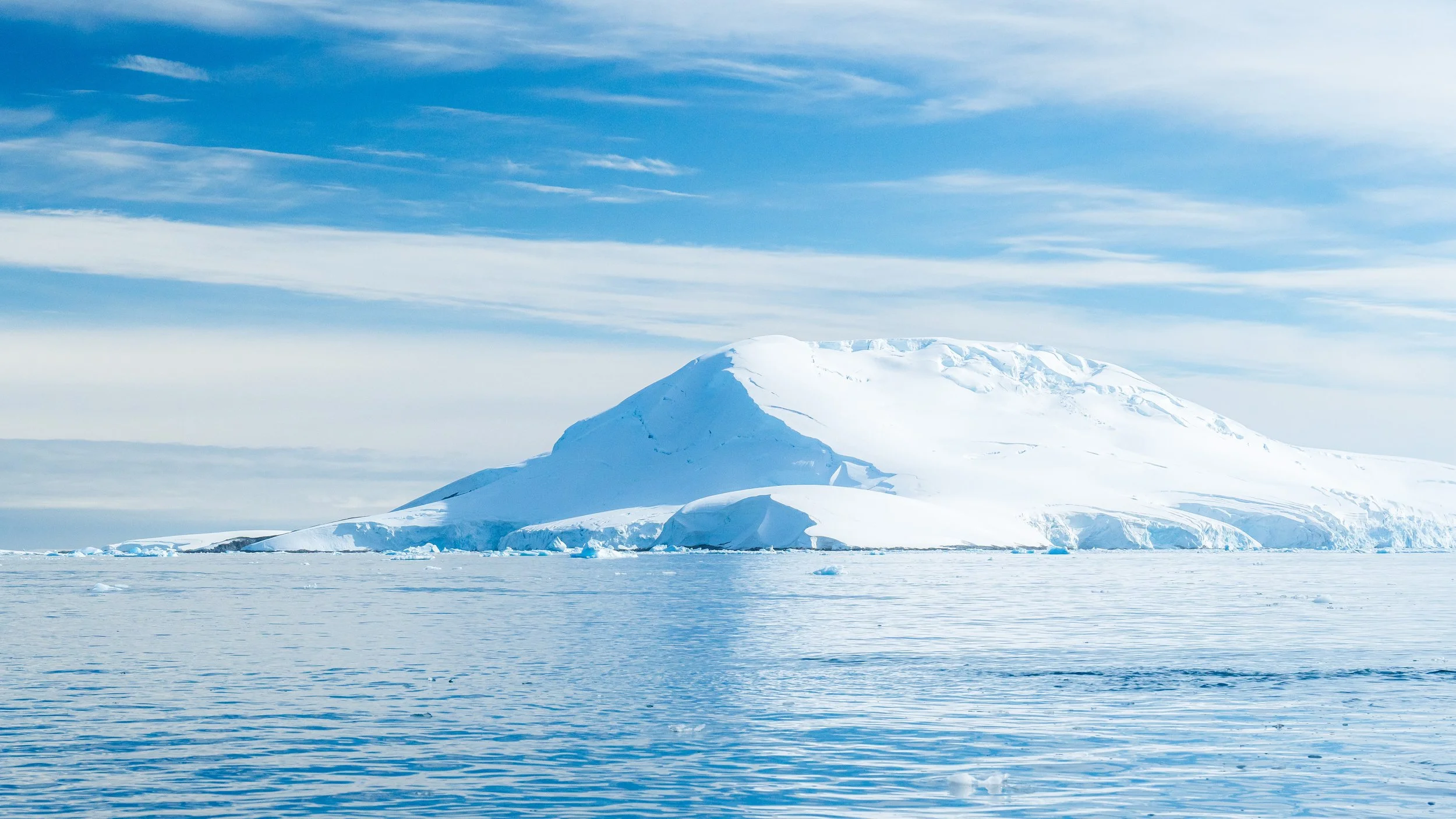 A large snow-covered iceberg floating in icy waters under a partly cloudy sky.
