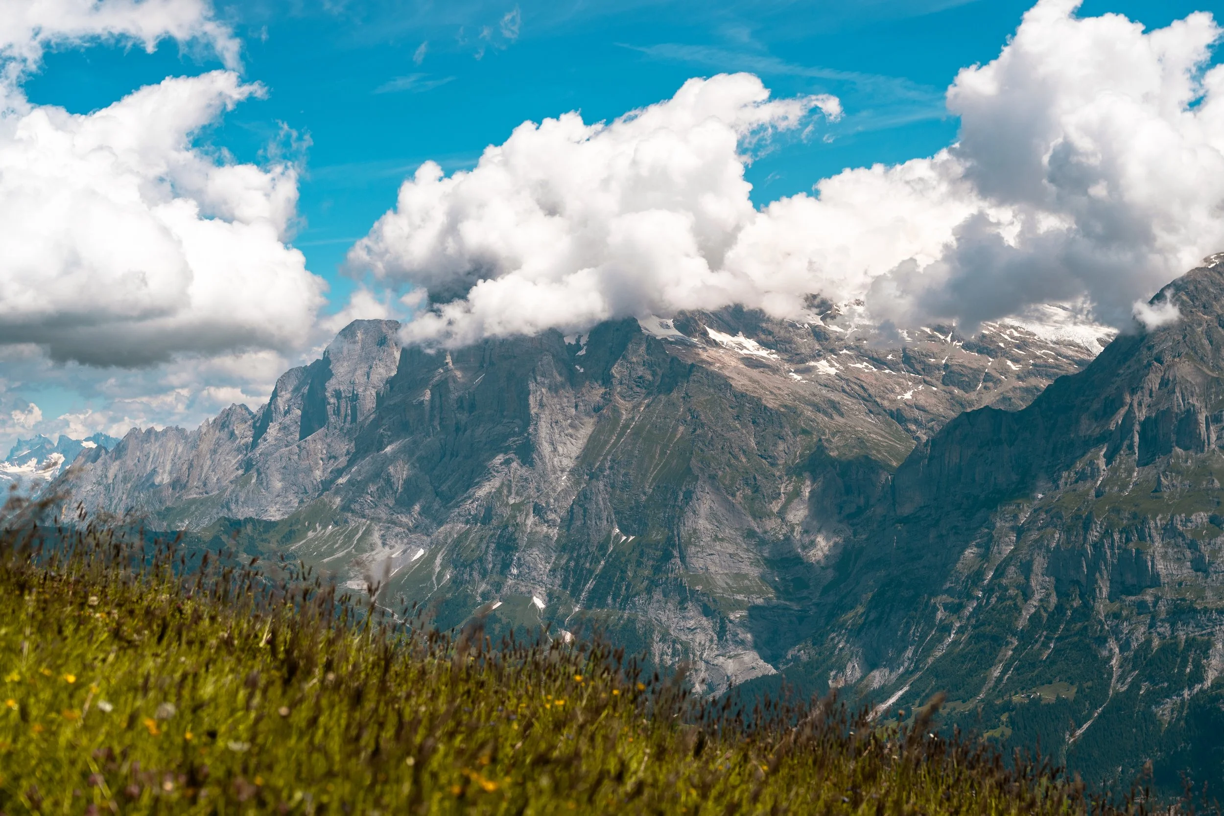 Scenic mountain landscape with rugged peaks, snow patches, and a partly cloudy blue sky.