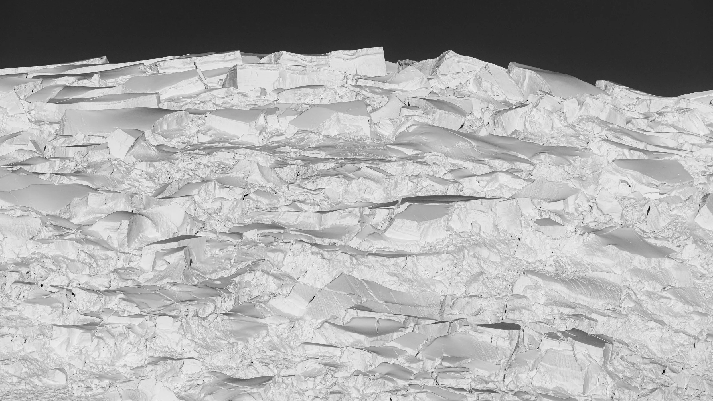 Black and white photo of a snow-covered landscape with jagged ice and snow formations, and a clear dark sky.
