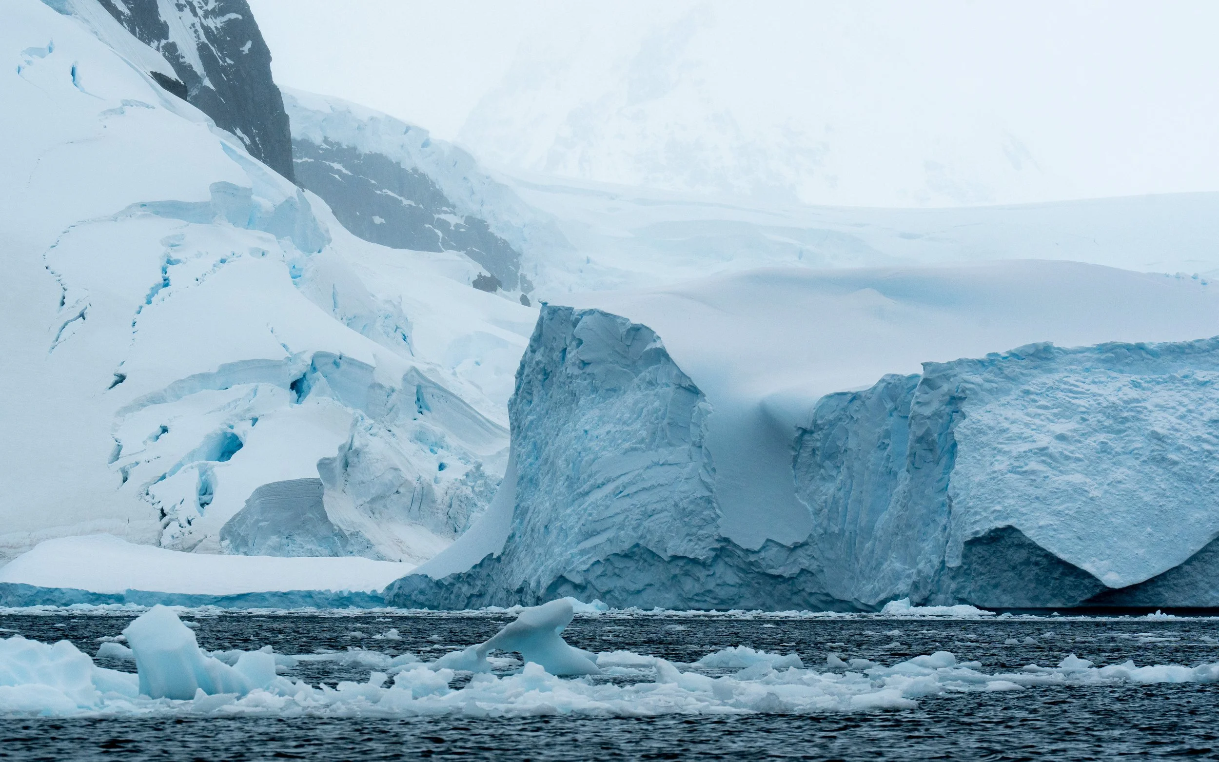 A frozen icy landscape with large ice formations and glaciers, and a body of water with floating ice chunks in the foreground.