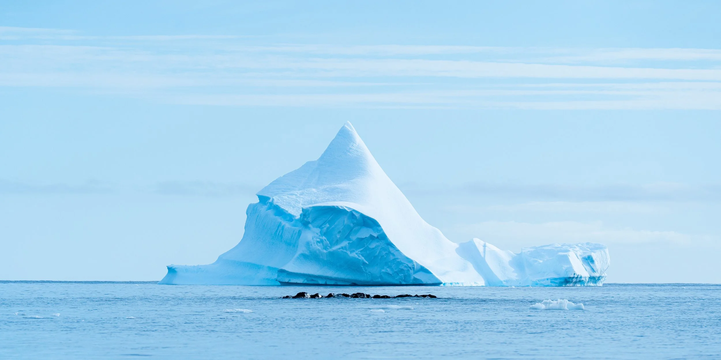 A large iceberg floating in the ocean with a clear blue sky overhead.