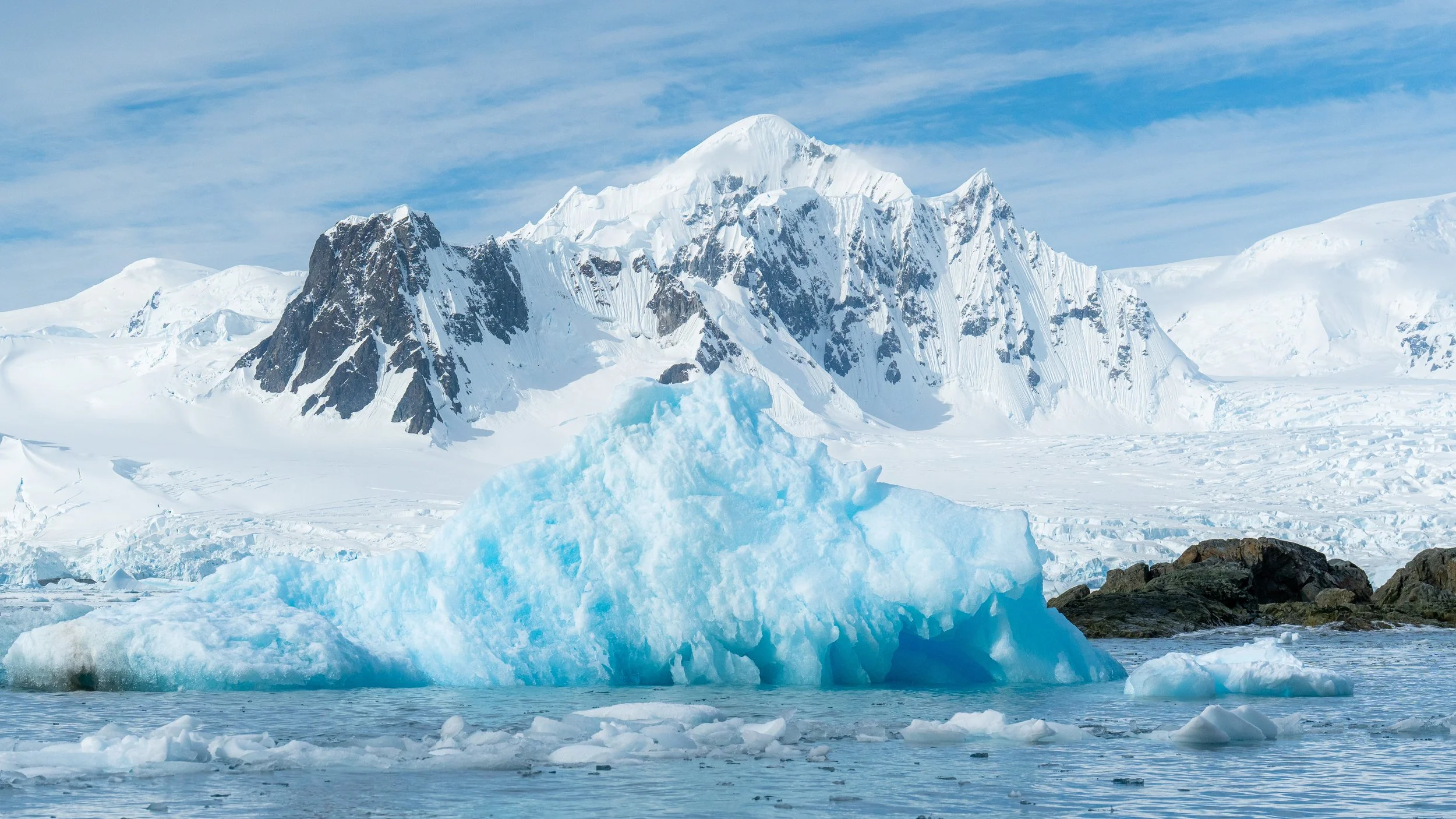 Snow-covered mountain range with large icebergs floating on the icy water in front.