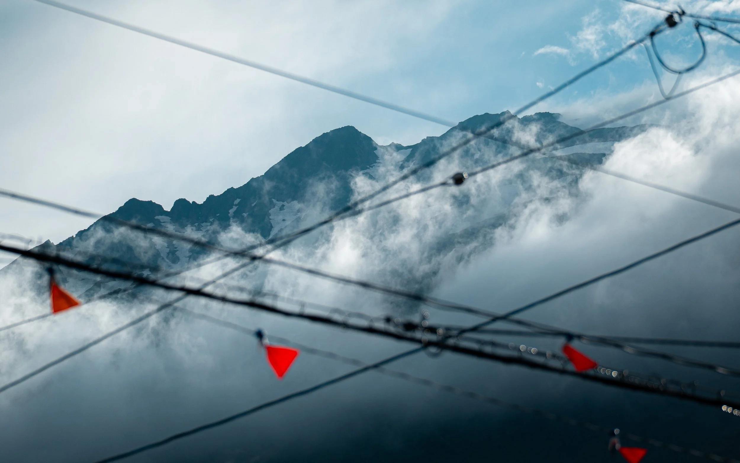 Mountains covered with snow and clouds, with some wires and red flags in the foreground.