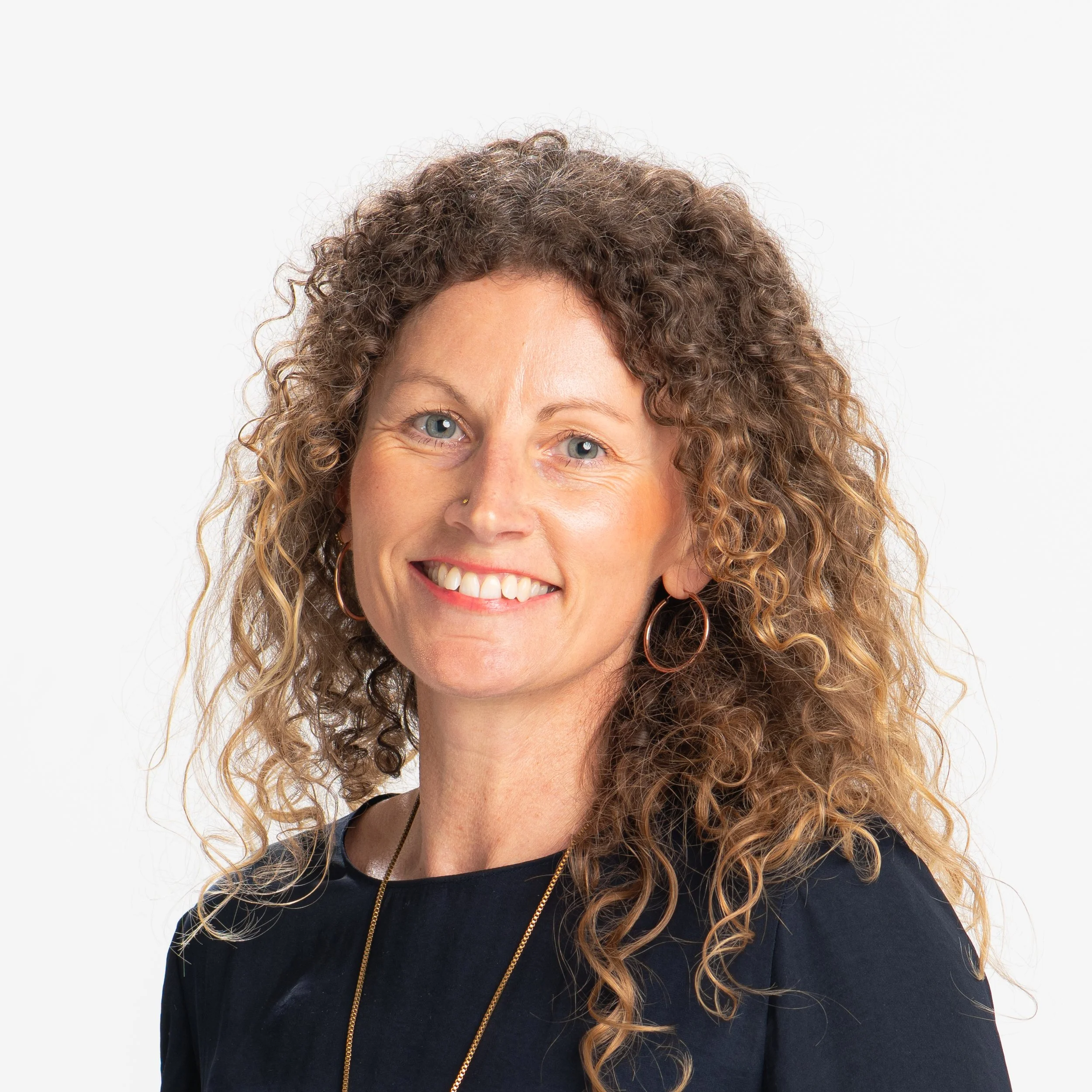 A woman with curly hair smiling and wearing a black shirt and gold necklace.