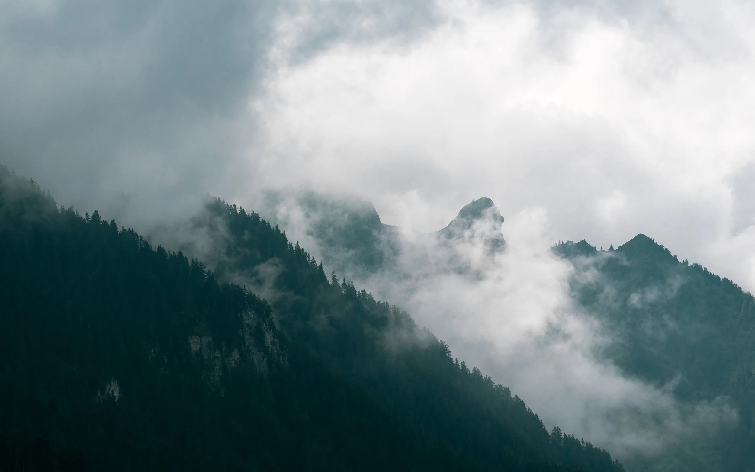 Mountains covered in dense forest with clouds and mist surrounding the peaks.