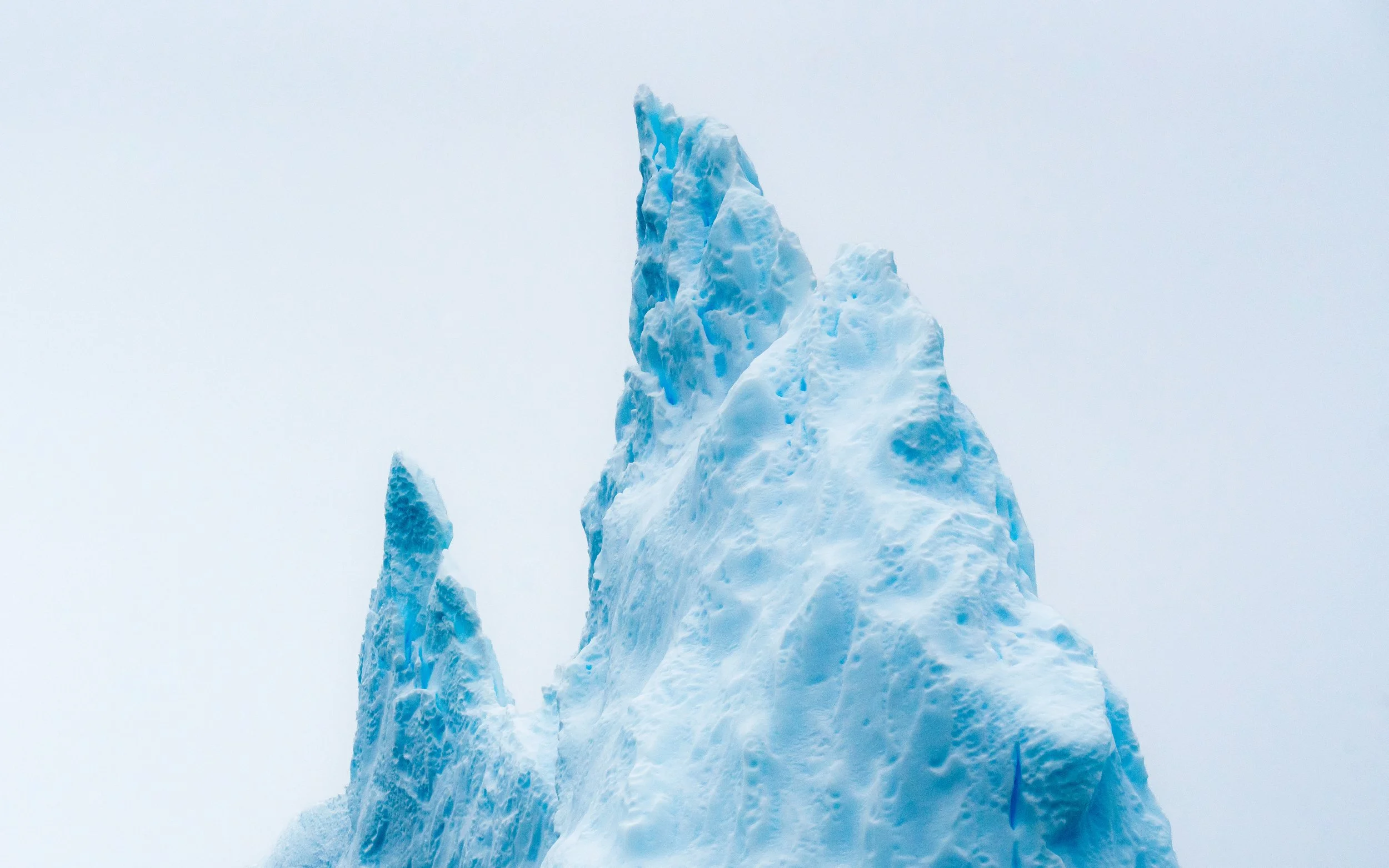 Tall, jagged iceberg with various shades of blue and white against a cloudy sky.