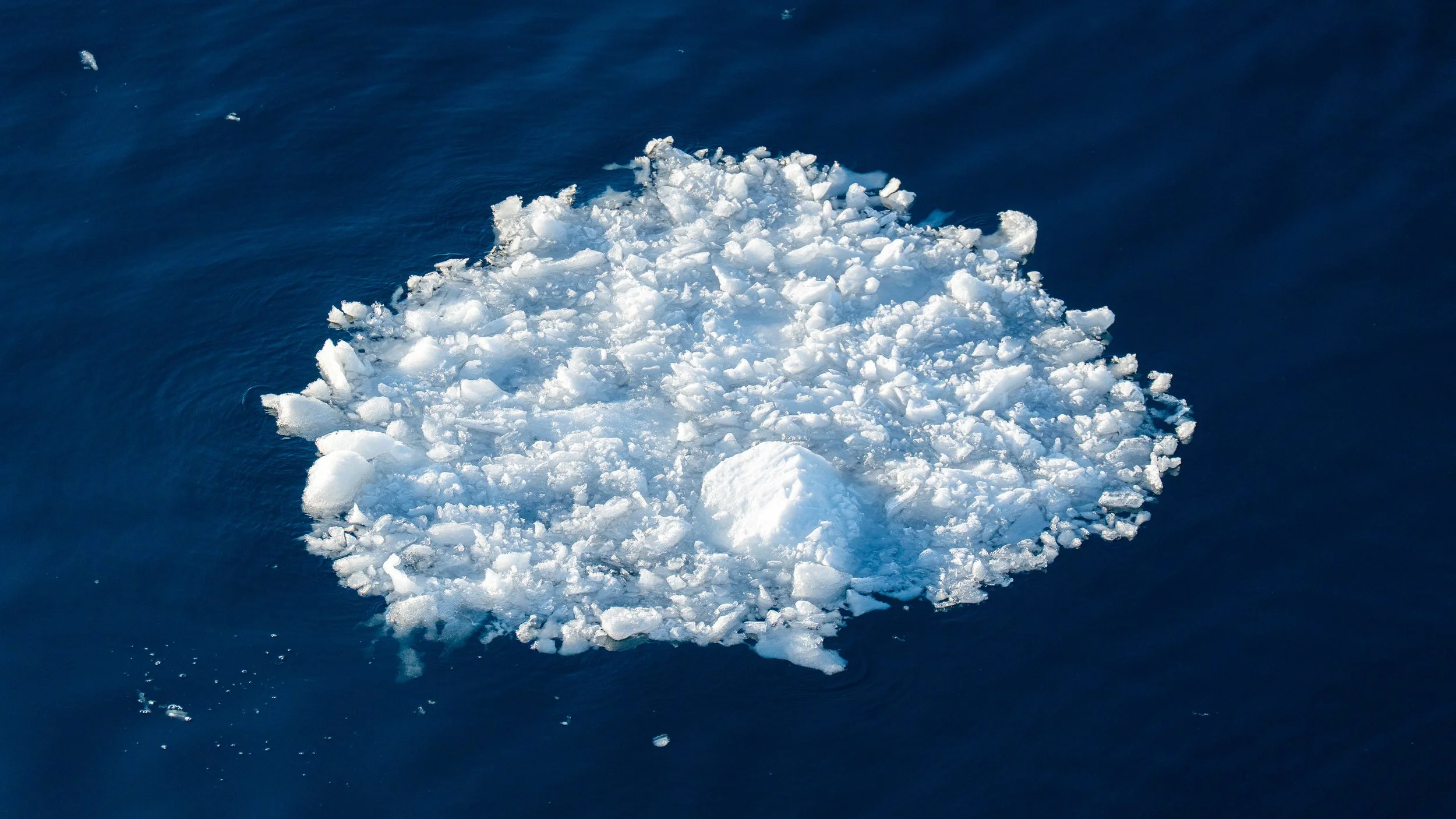 A large ice formation floating on dark blue water.