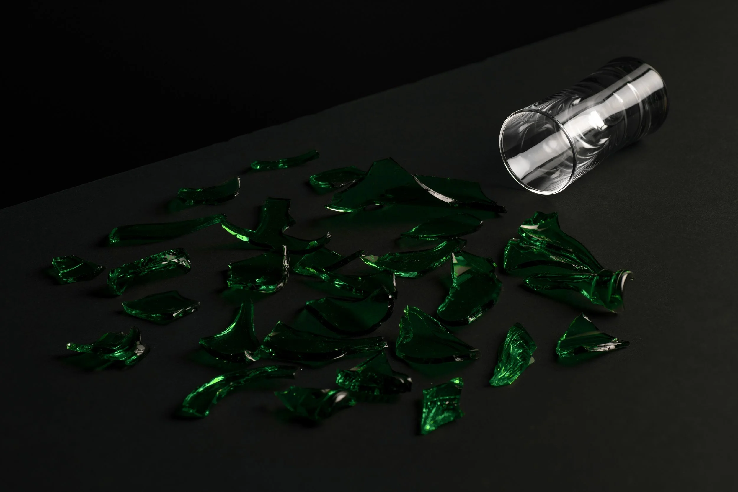 Broken glass with green tint spilled on black surface, frosted glass tube lying on side.